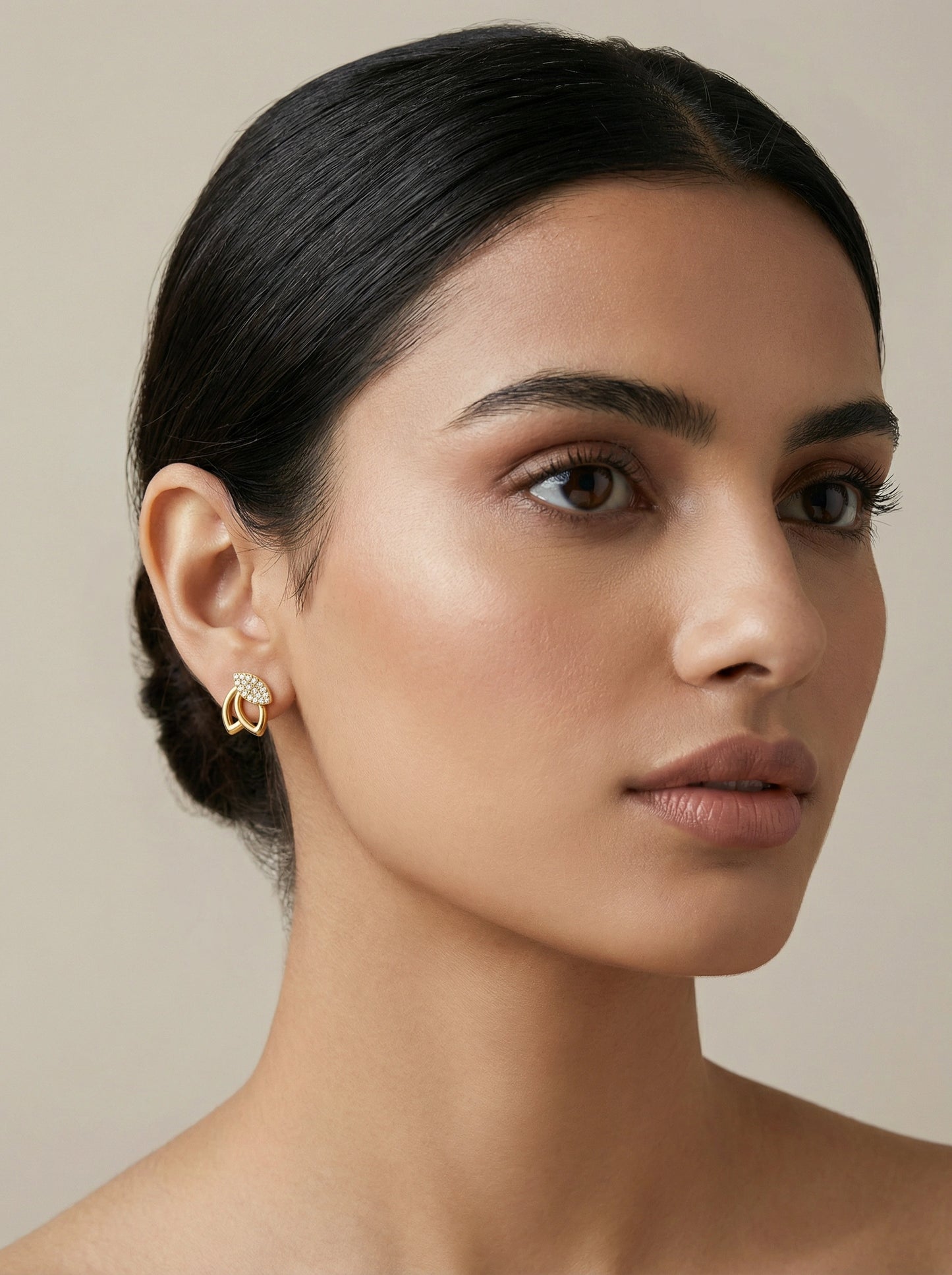 close-up of a woman wearing 18k gold plated hoop earrings against a neutral background