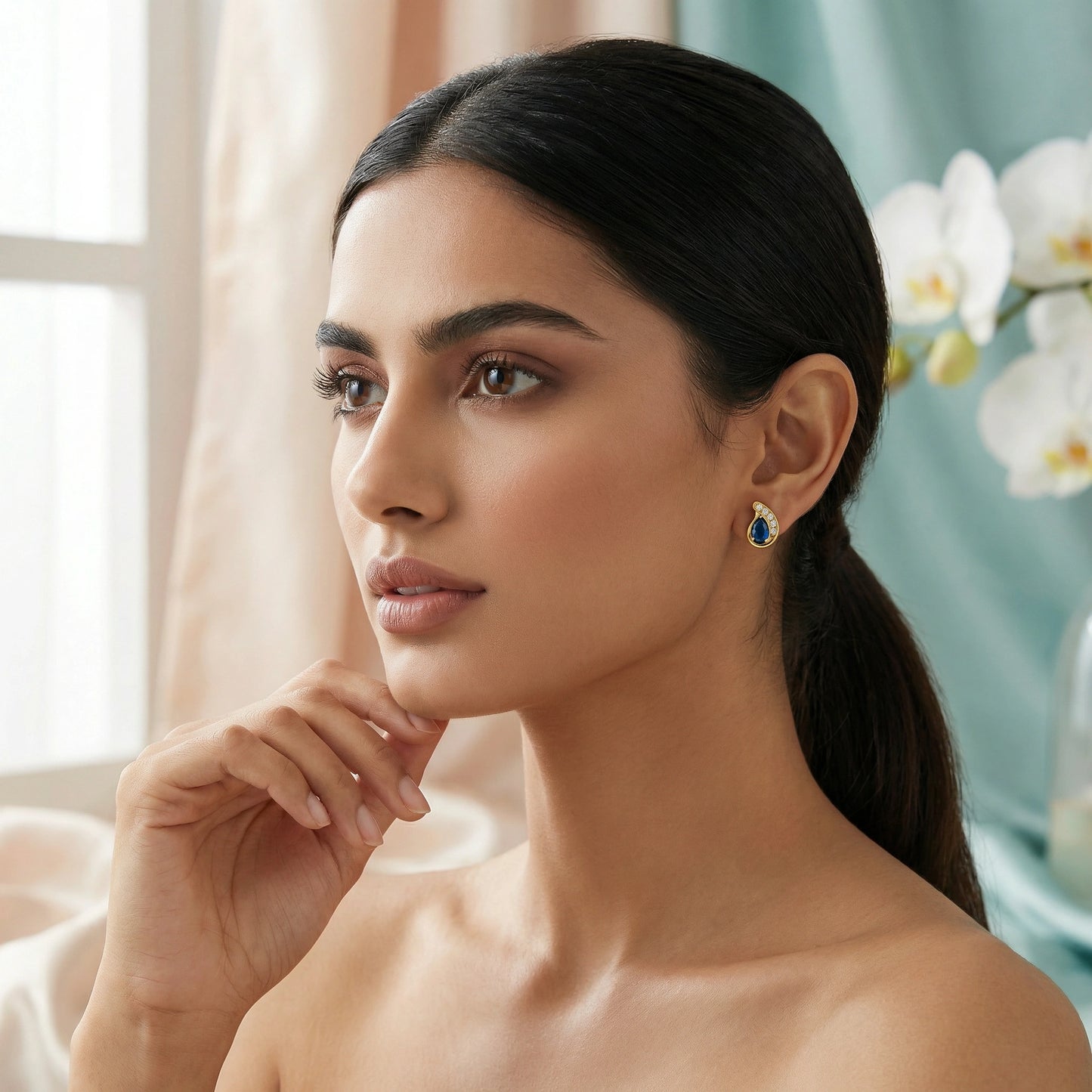 woman wearing a blue 18k gold plated earring in a softly lit room with flowers in the background