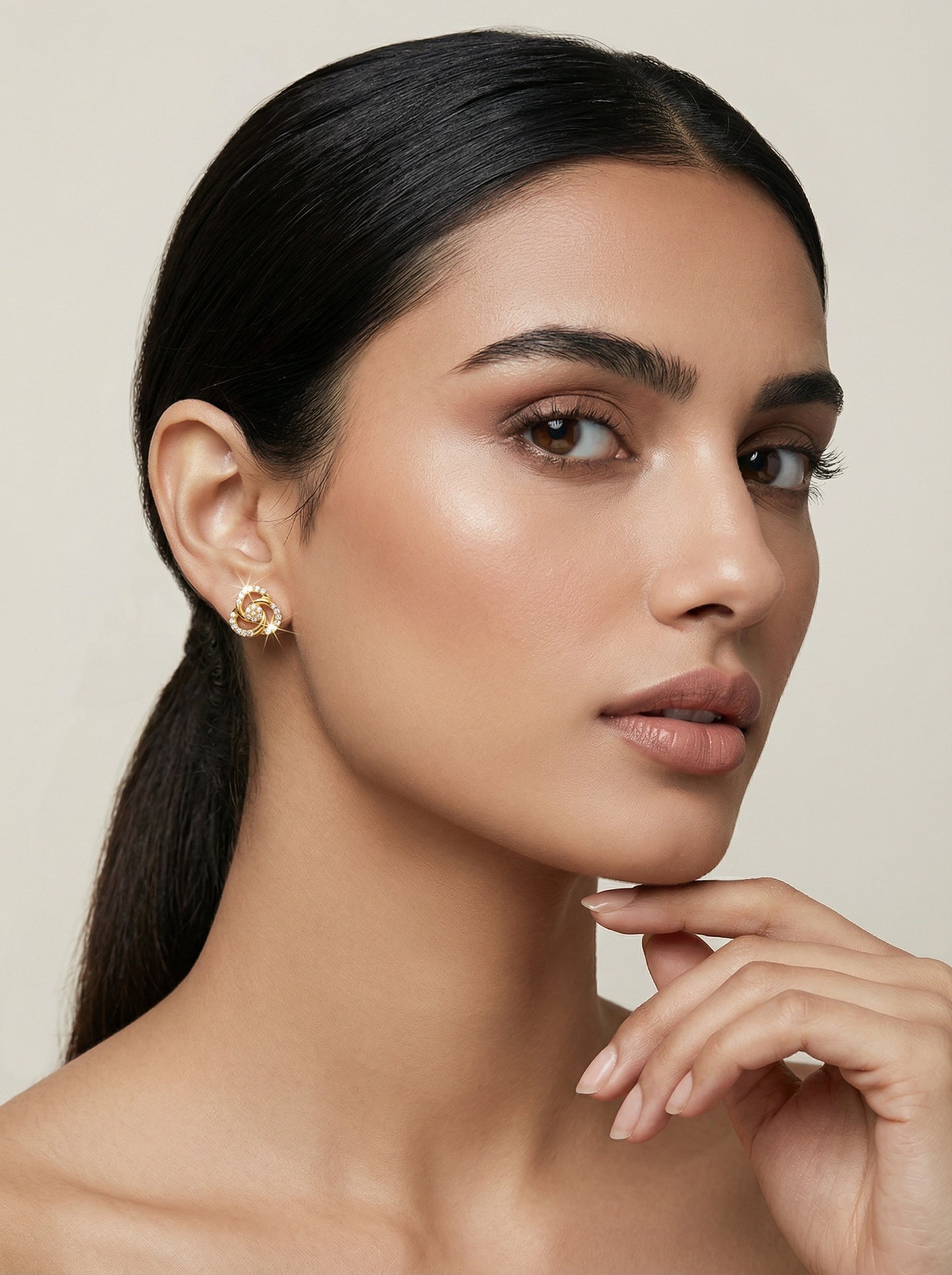 woman with a ponytail wearing 18k gold plated earrings against a neutral background