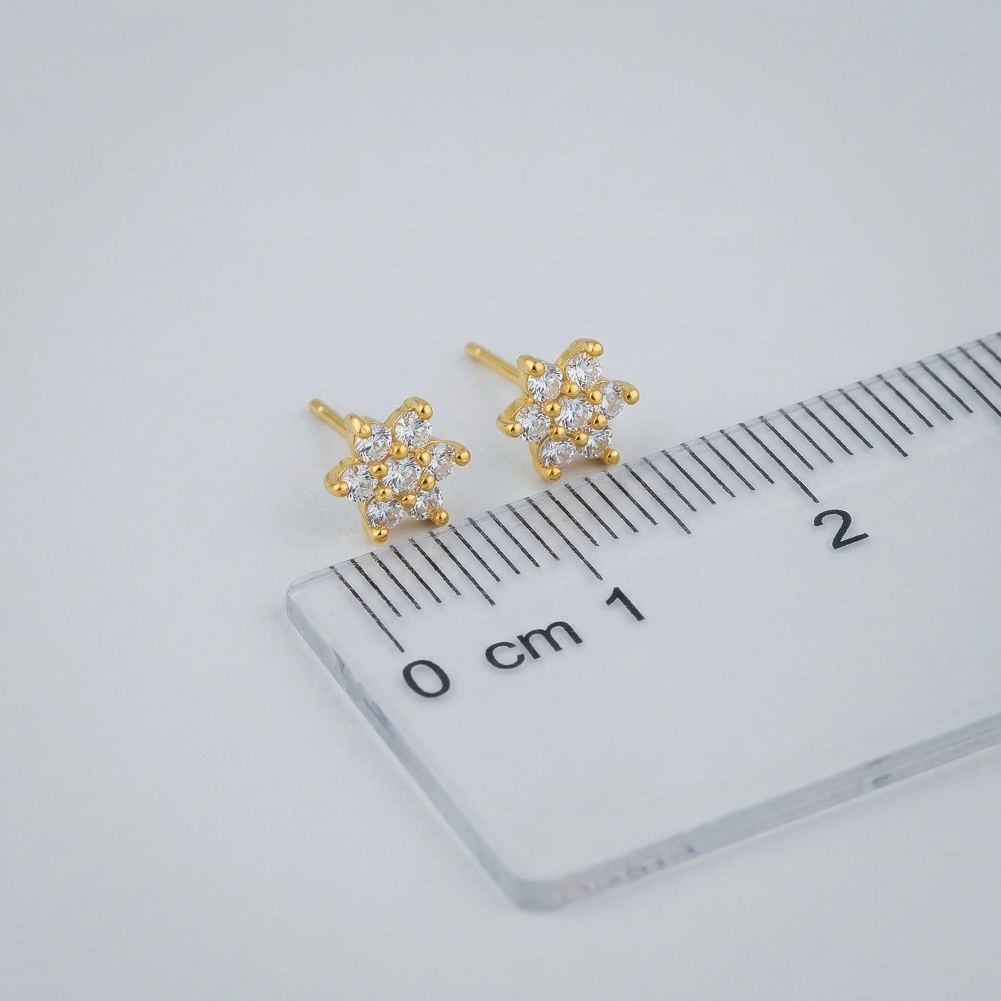 18k gold plated arrings with clear stones on a ruler for scale, on a light gray background