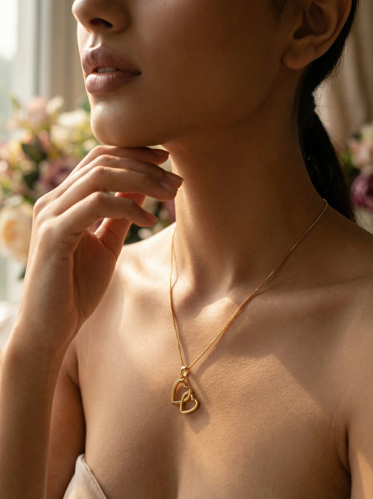 woman wearing a 18k gold plated necklace with a heart pendant, with a blurred floral background
