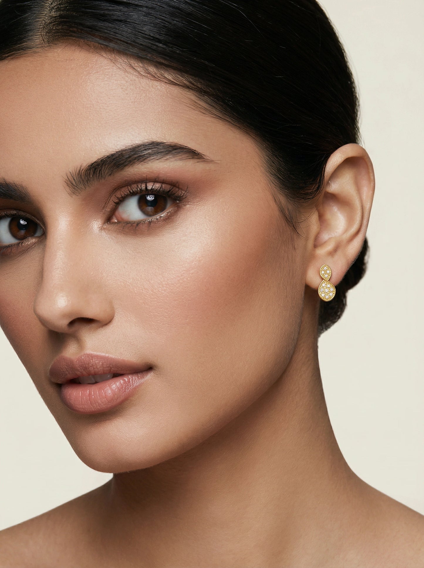 close-up of a woman wearing 18k gold plated earrings with a neutral background