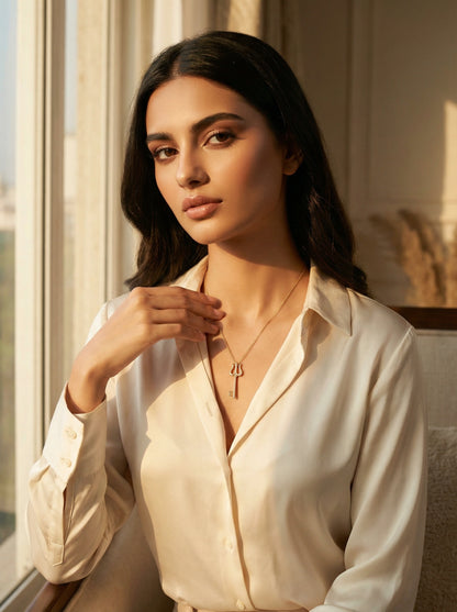 Woman wearing a white blouse and 18k gold plated necklace in a softly lit room.