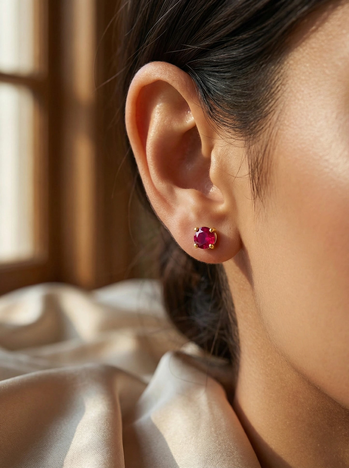 close-up of an ear wearing a  18k gold plated red gemstone earring with a soft background