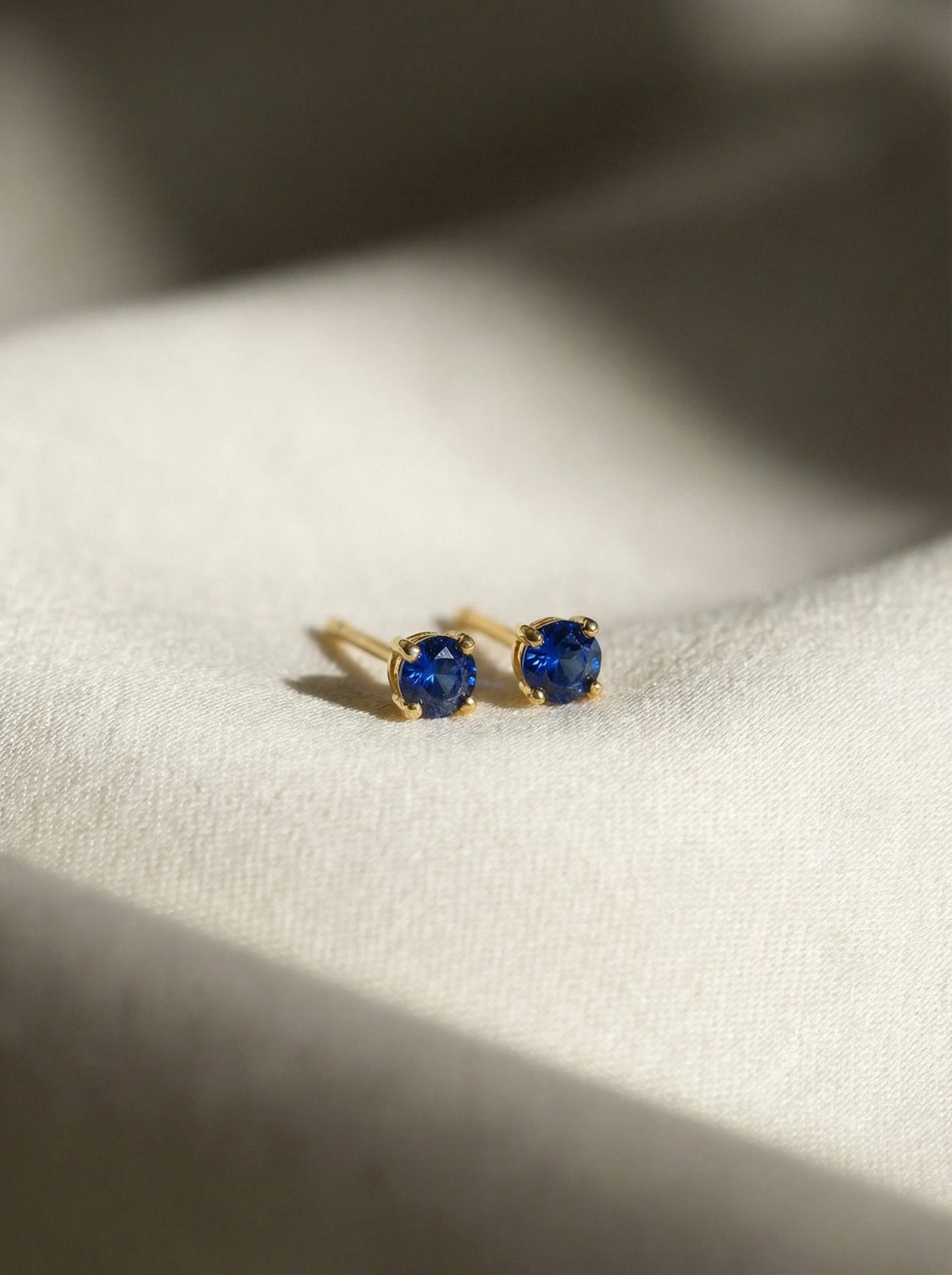 18k gold plated earrings with blue gemstones on a white fabric background