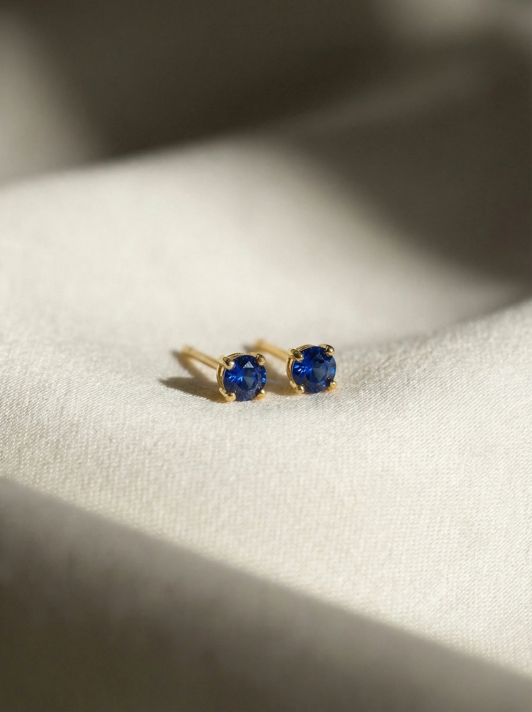 18k Gold plated earrings with blue gemstones on a white fabric background
