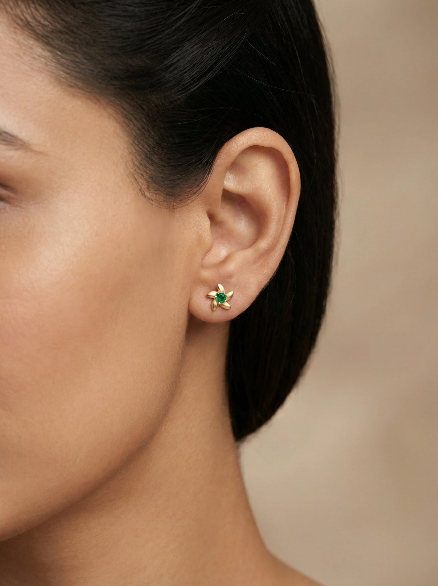 close-up of a person wearing a 18k gold plated green gemstone earring with a blurred background