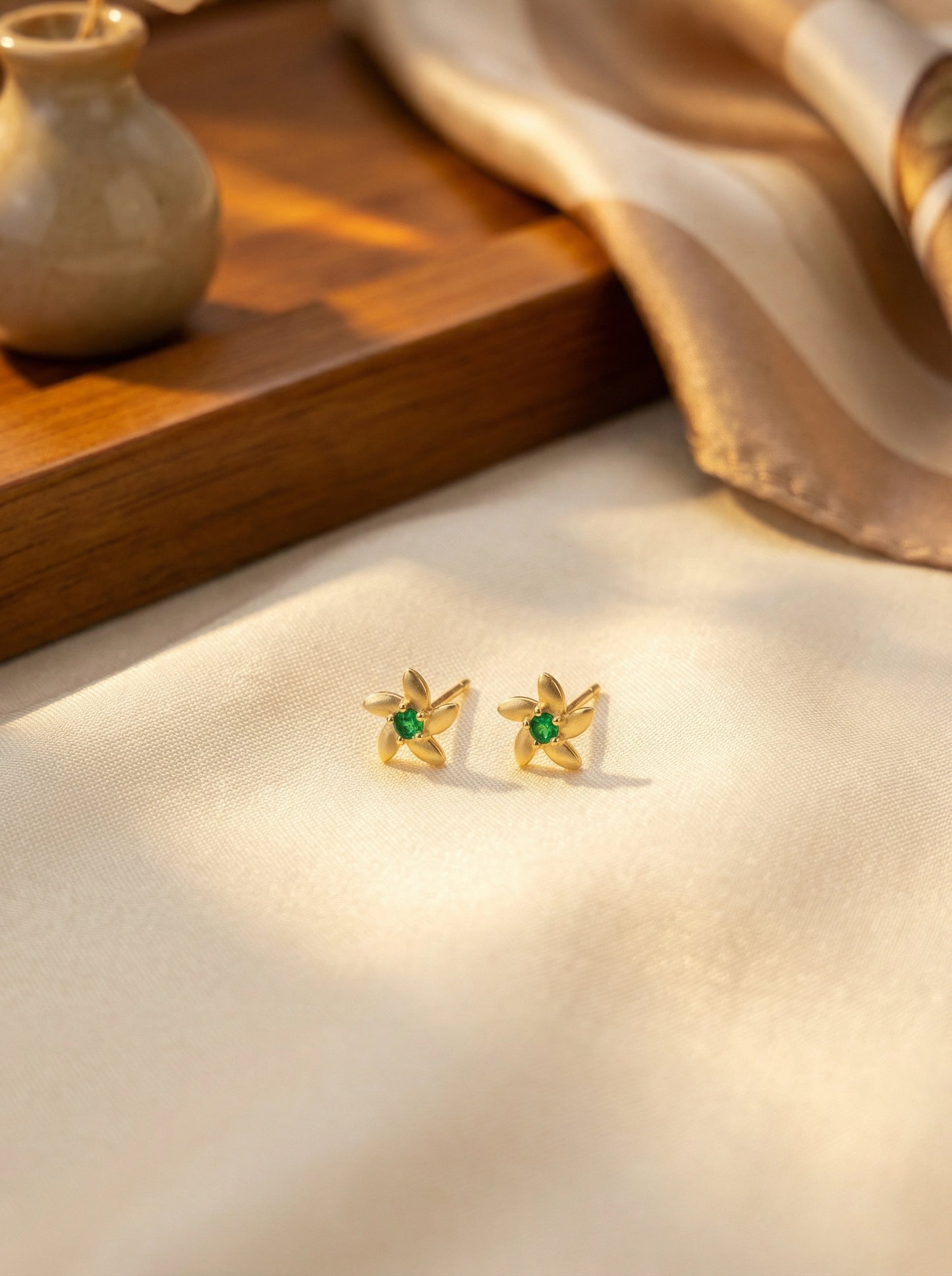 18k gold plated earrings with green gemstones on a soft fabric background