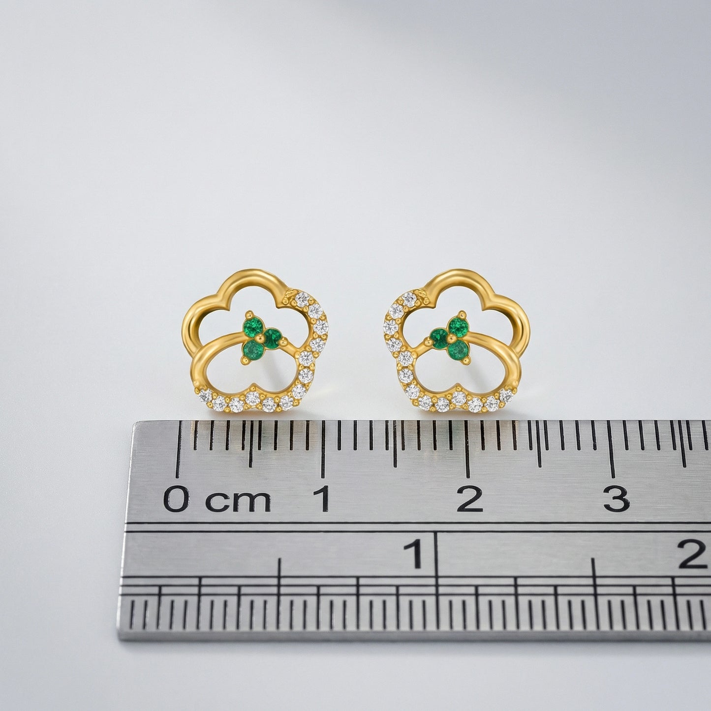 18k gold plated earrings with green gemstones and clear stones on a ruler for scale.