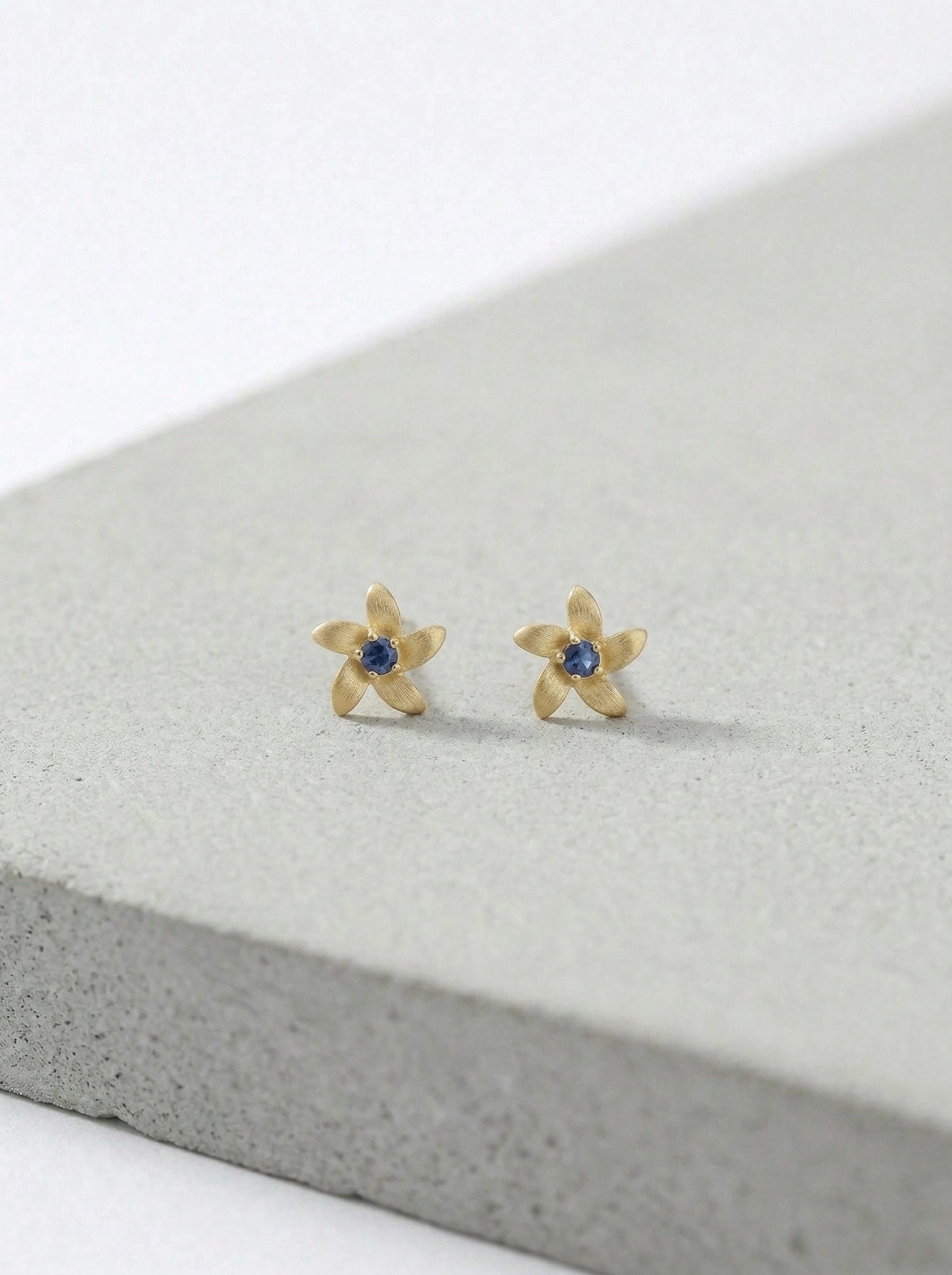 18k gold plated flower-shaped earrings with blue stones on a gray surface