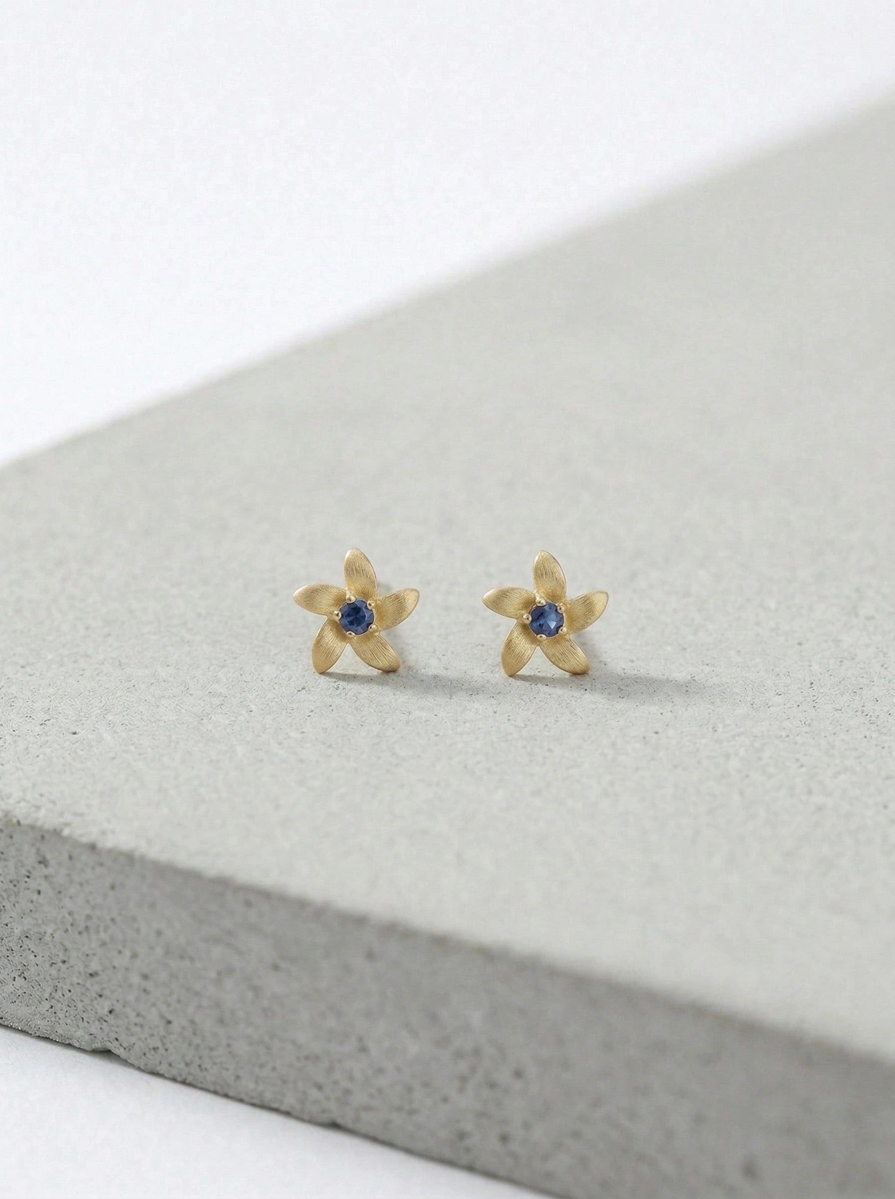 18k Gold plated flower-shaped earrings with blue stones on a gray surface