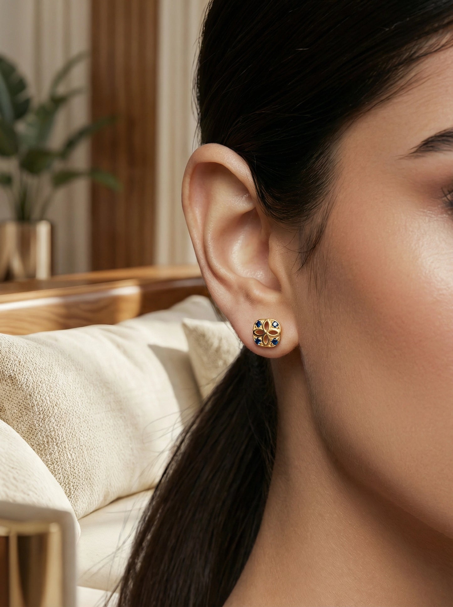 close-up of a person wearing a 18k gold plated earring with a blurred indoor background