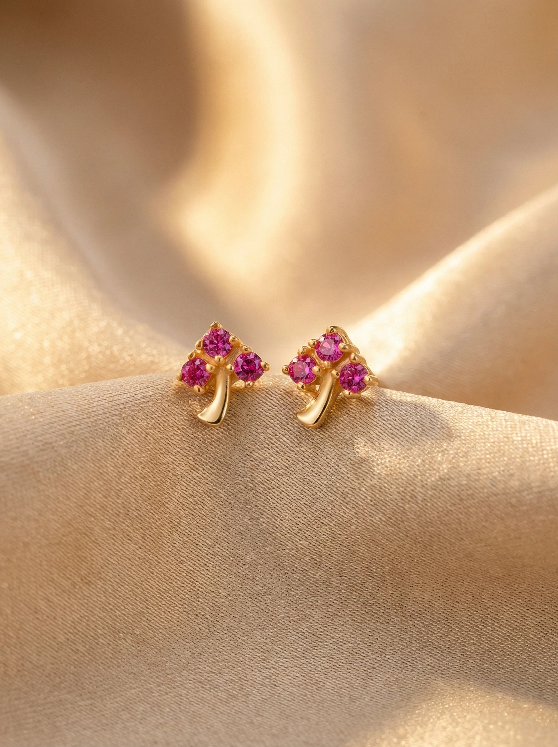 18k Gold plated earrings with pink gemstones on a beige fabric background