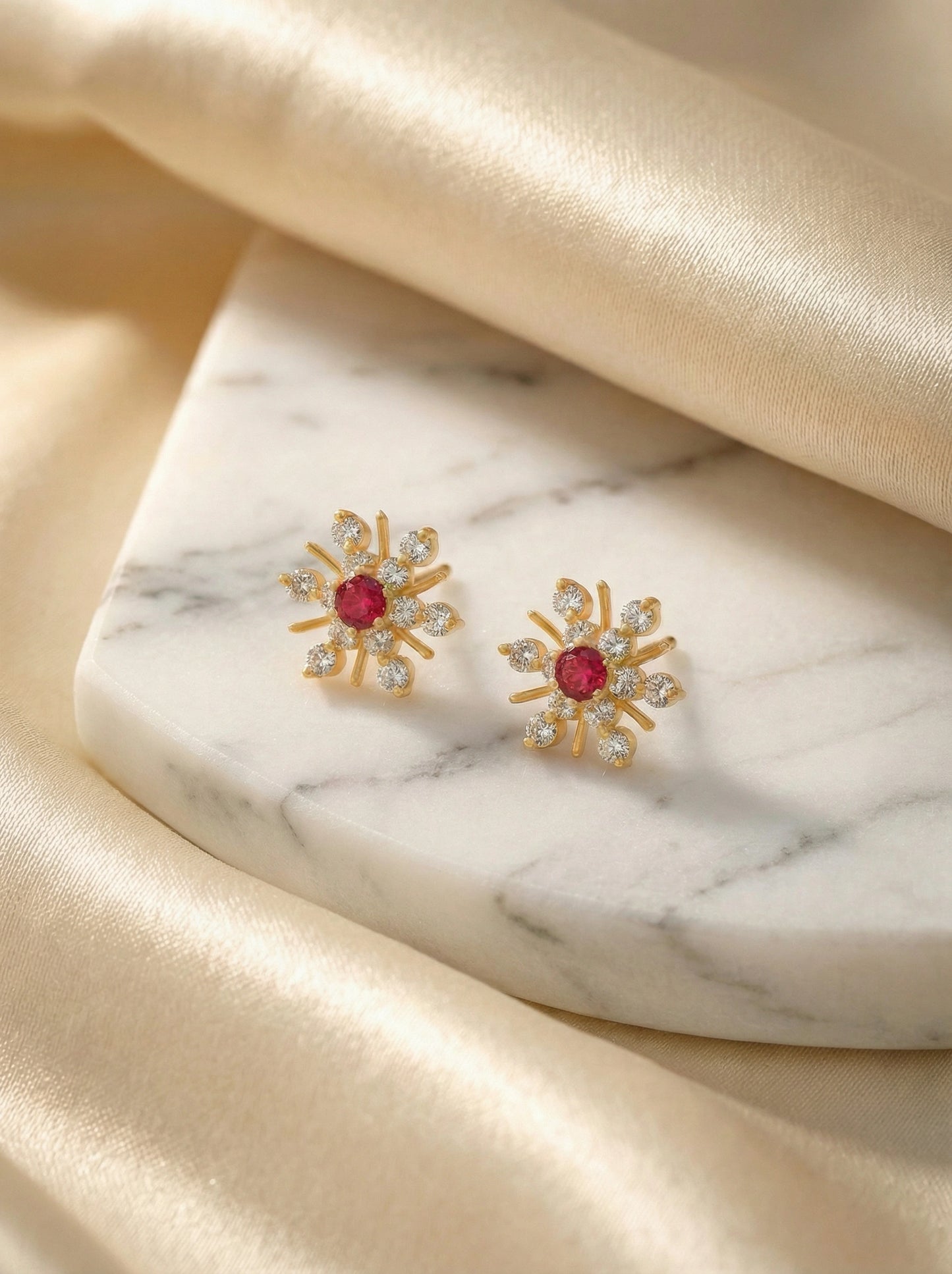 18k gold plated earrings with red gemstones on a marble surface