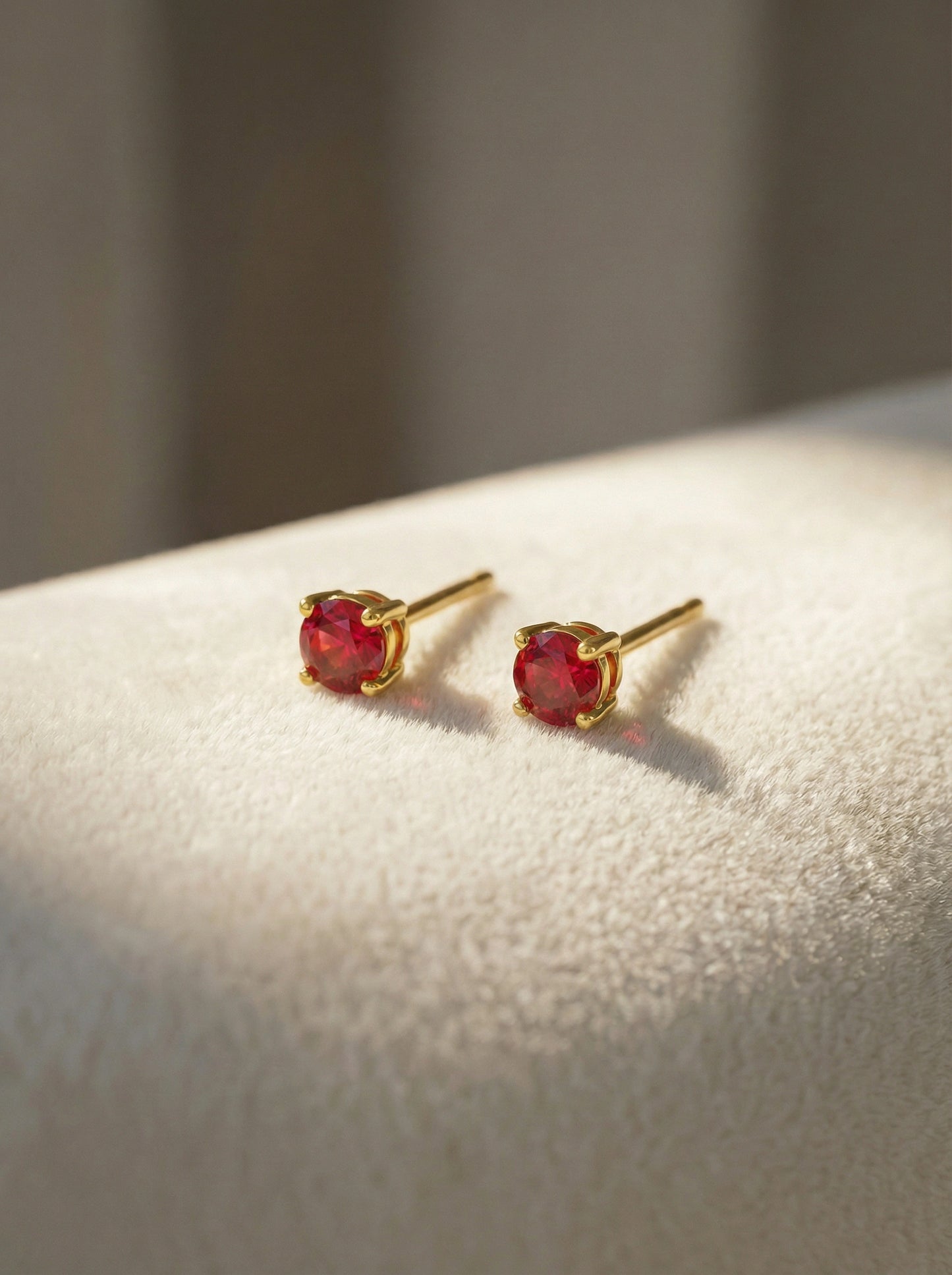 18k gold plated earrings with red gemstones on a light surface