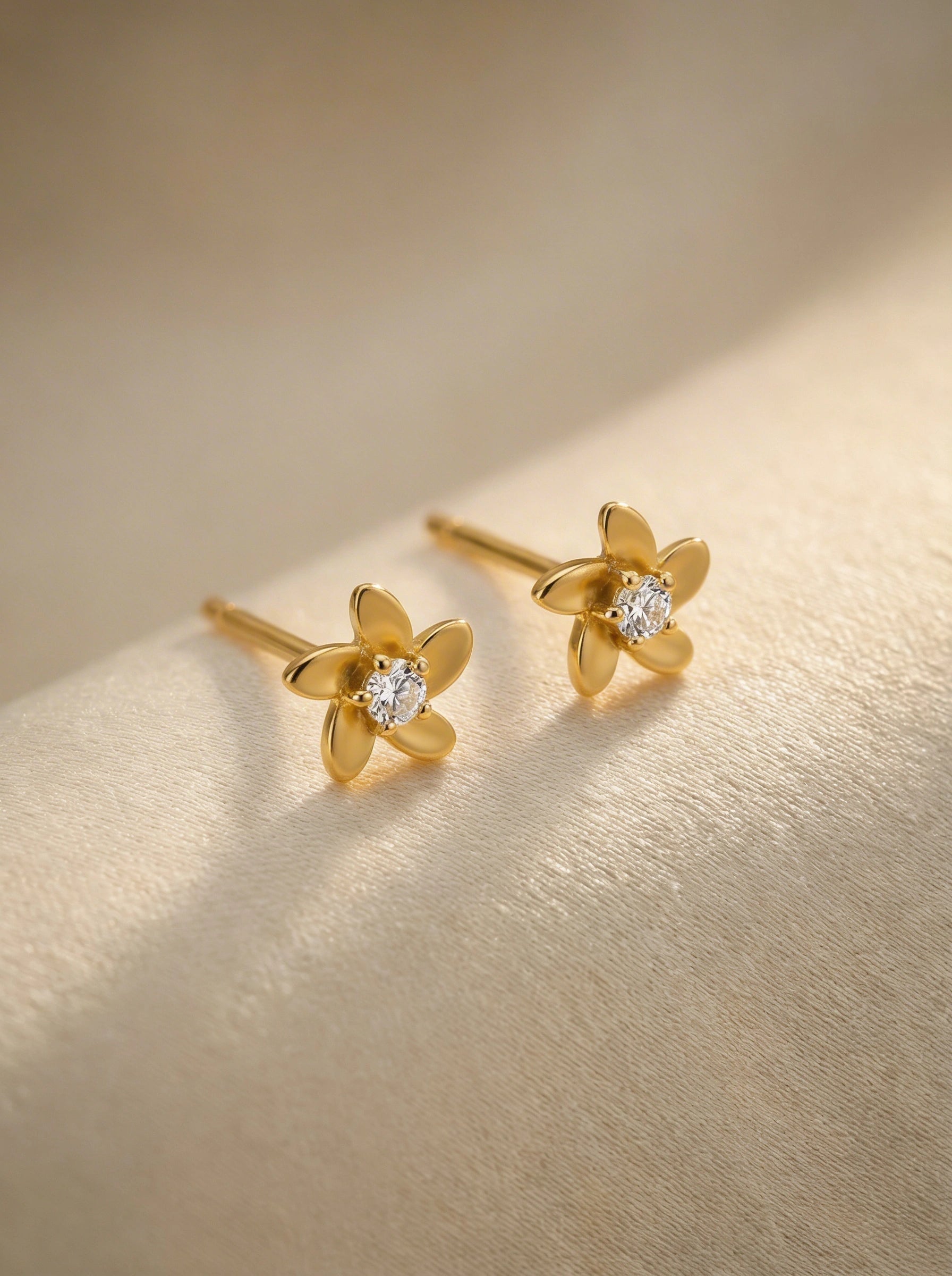  18k Gold plated flower-shaped earrings with diamond centers on a gold background