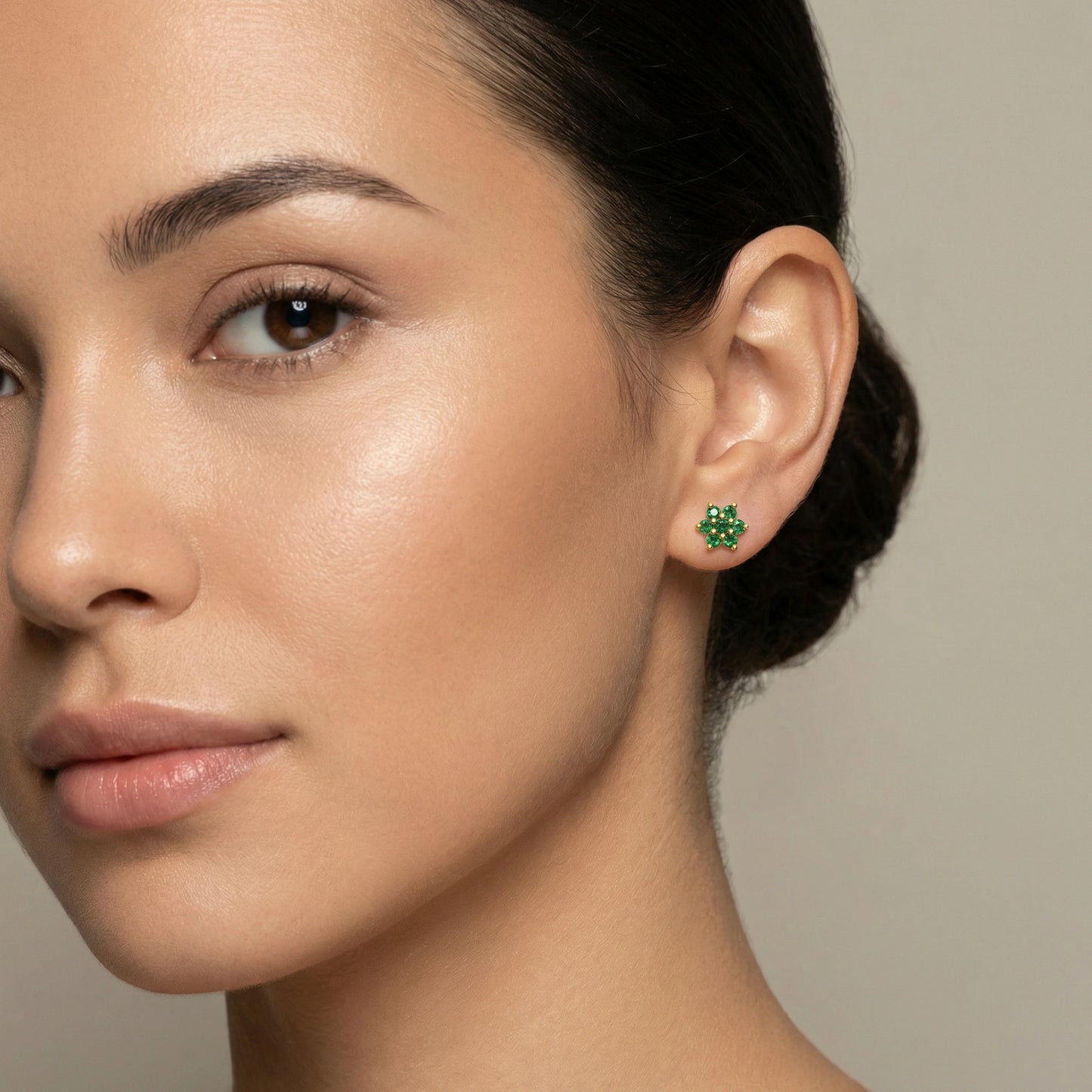 close-up of a woman wearing green 18k gold plated earrings with a neutral background