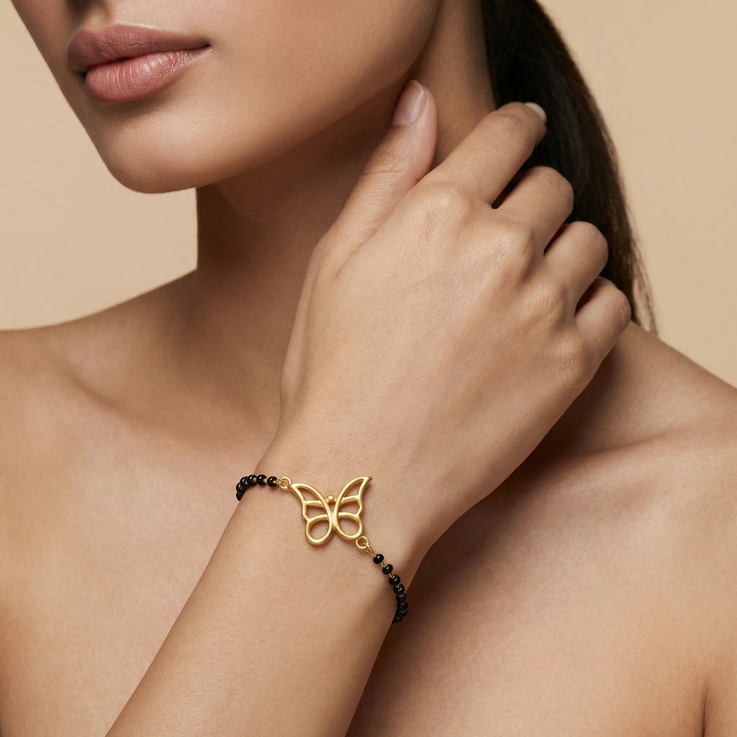 18k gold plated butterfly bracelet with black beads on a woman's wrist against a beige background