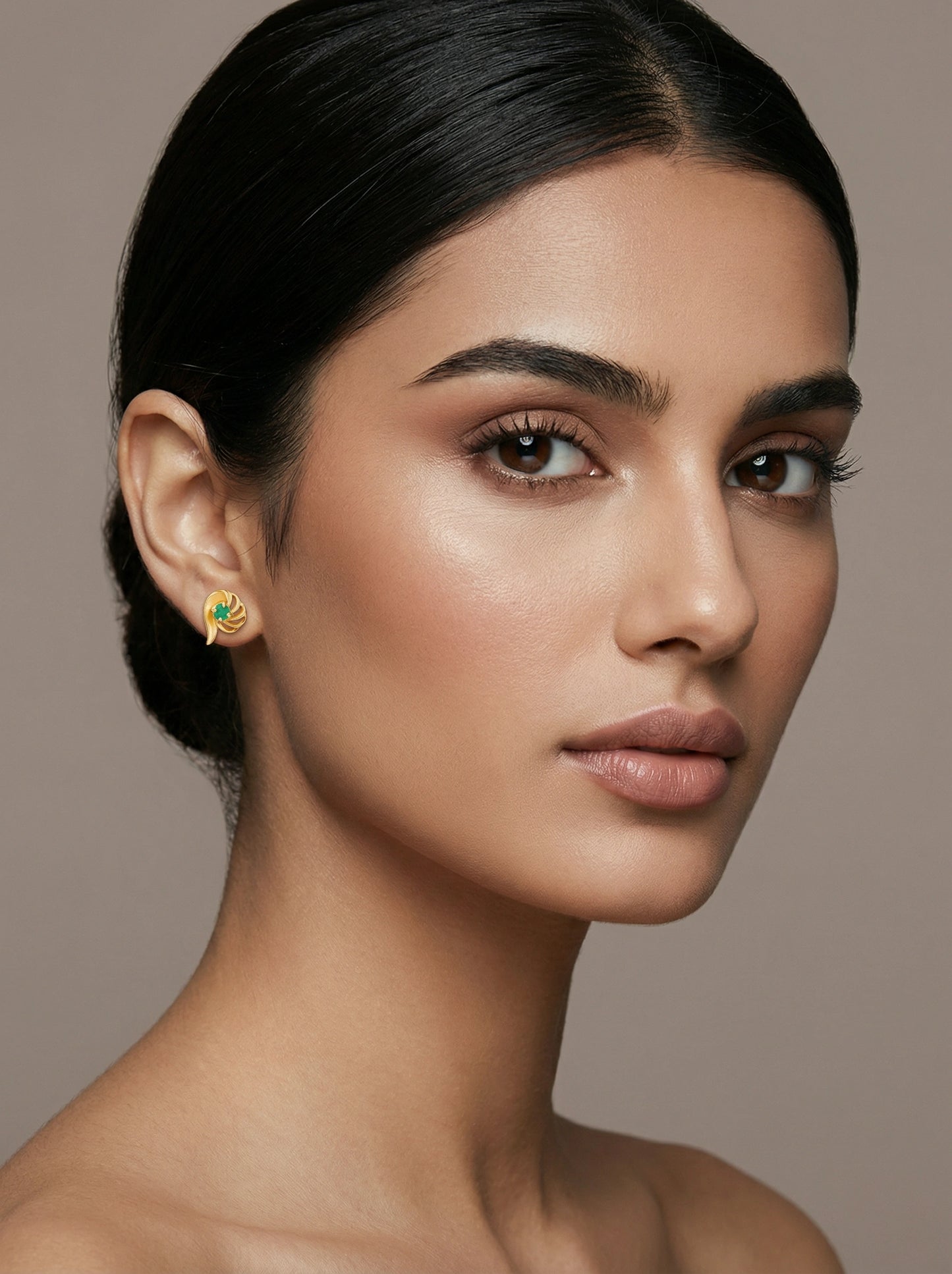 close-up of a woman wearing a 18k  gold plated earring with a green gemstone on a neutral background