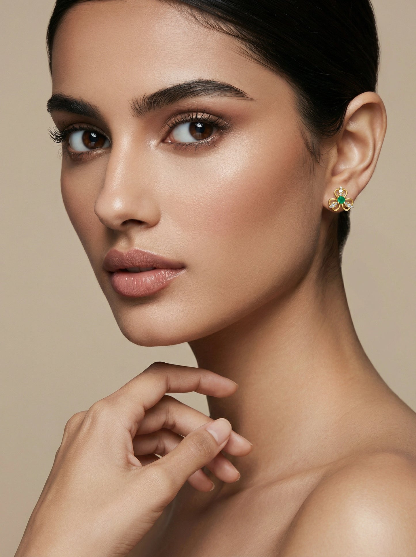 close-up of a woman wearing a 18k gold plated  green gemstone earring against a beige background