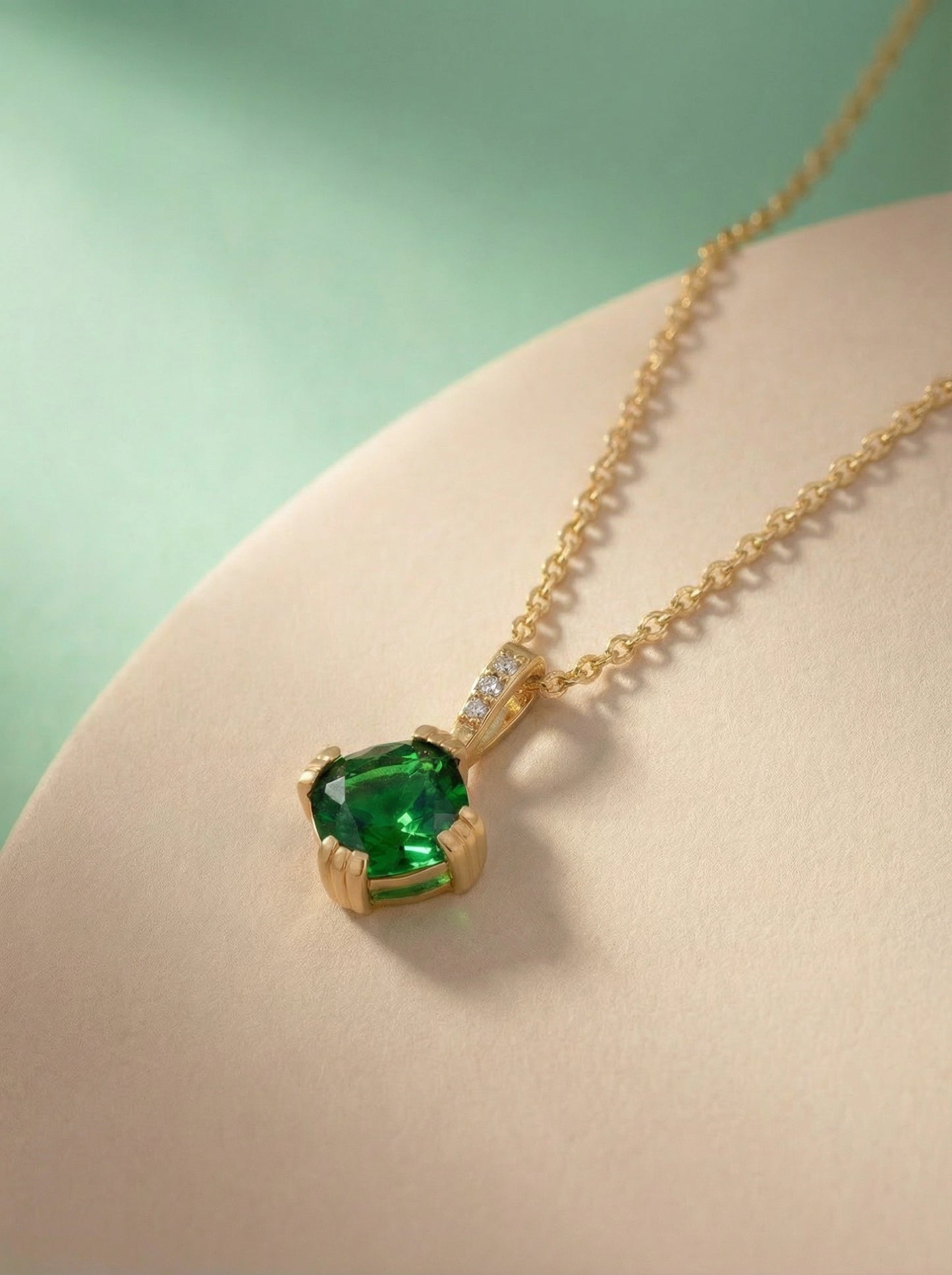 18k gold plated necklace with a green gemstone pendant on a light pink surface.