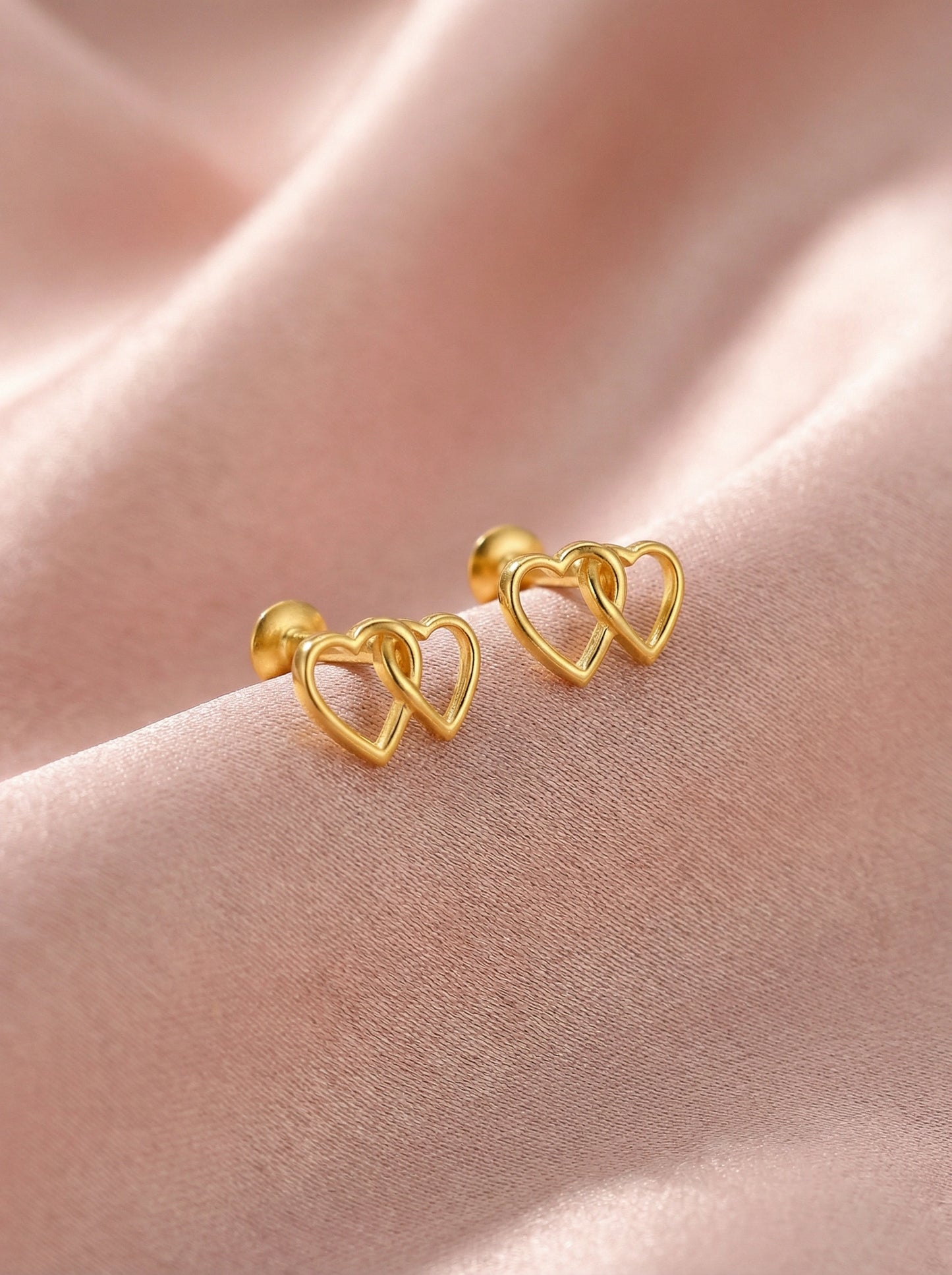 18k gold plated heart-shaped earrings on a pink fabric background