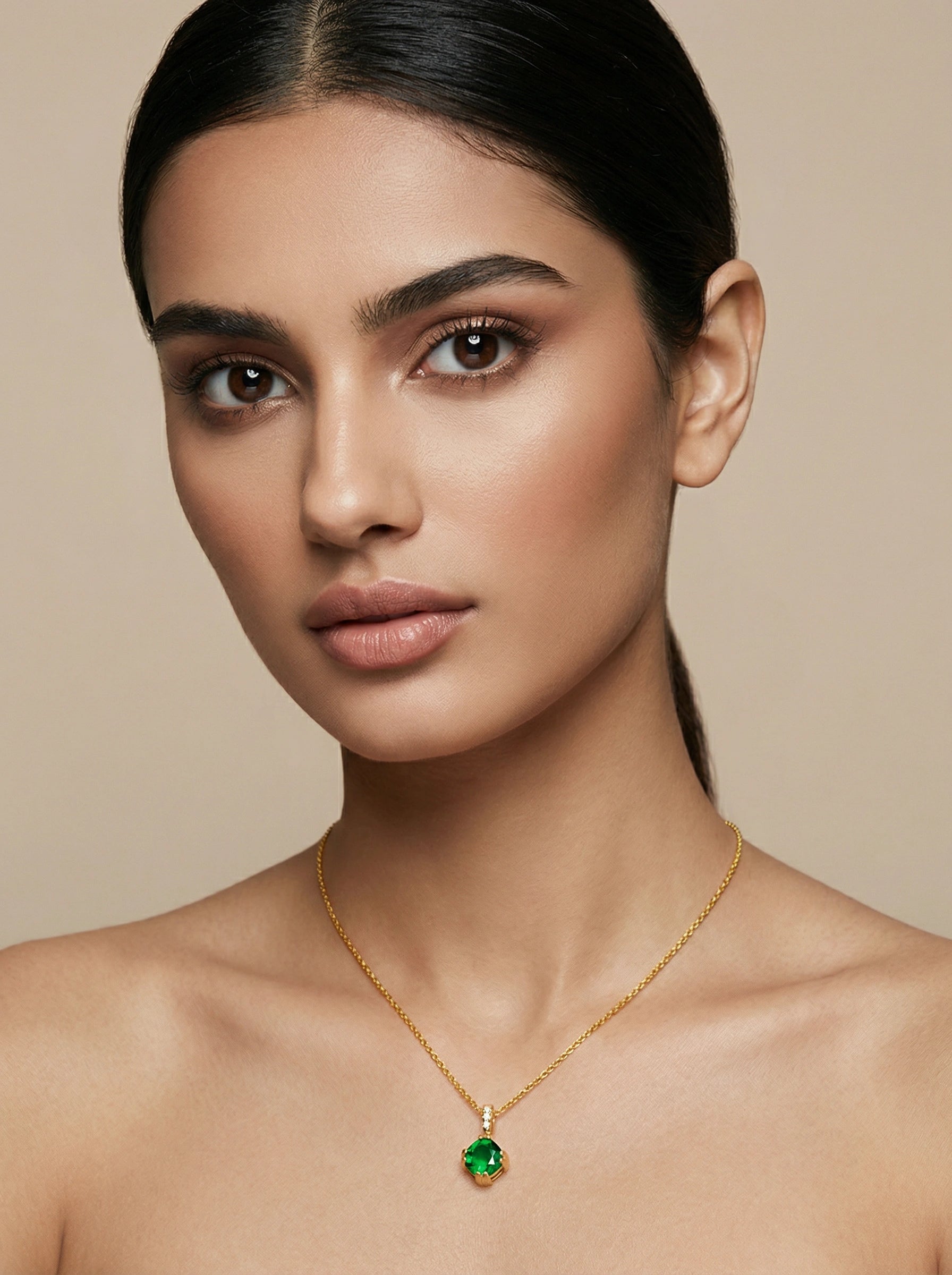 Woman wearing a 18k  gold plated necklace with a green pendant against a beige background