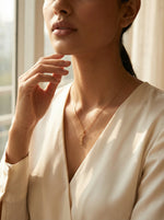 Woman wearing a delicate 18k gold plated necklace in a softly lit room