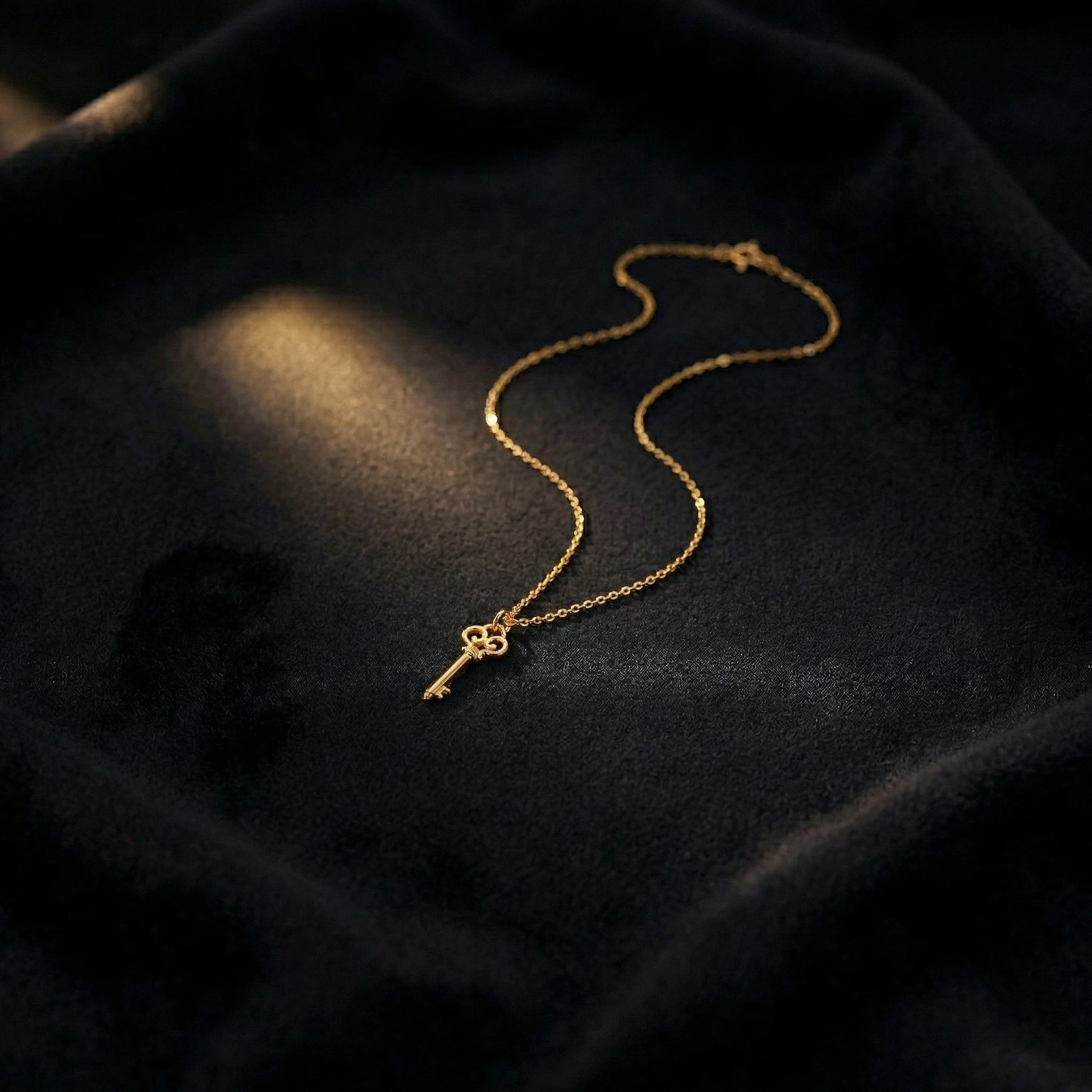 18k Gold plated key necklace on a dark fabric background