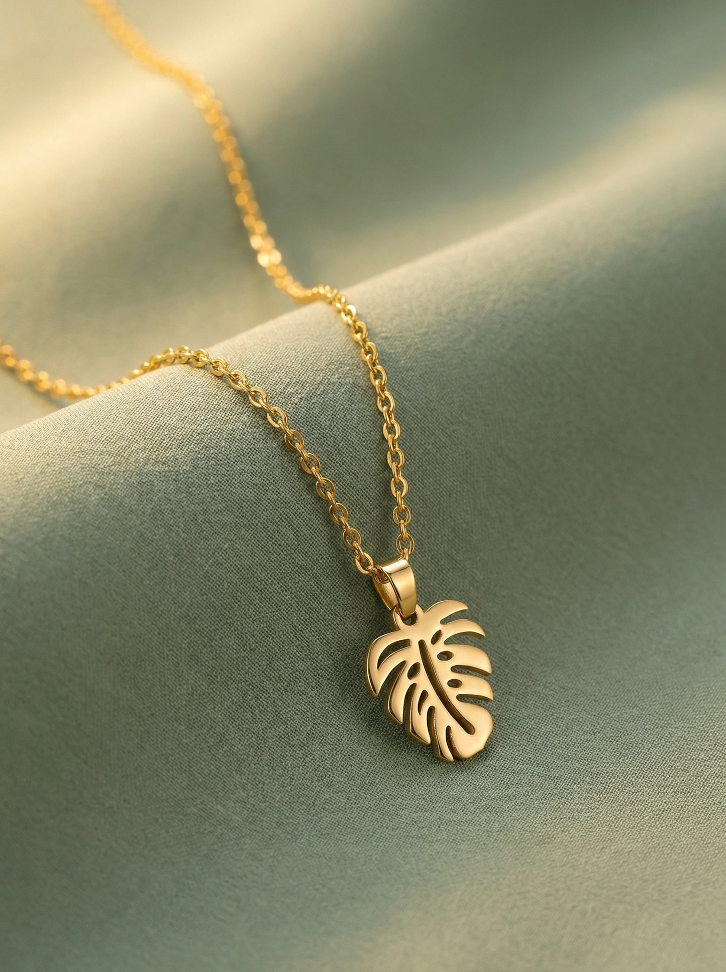 18k gold plated necklace with a leaf pendant on a soft green fabric background