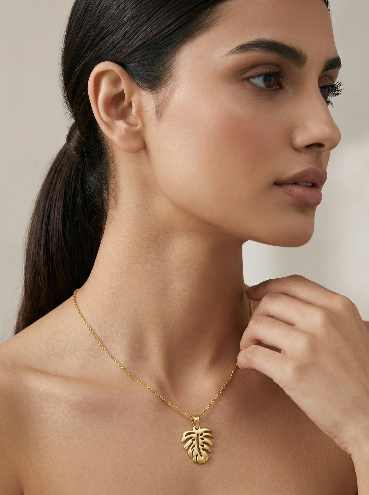 woman wearing a 18k gold plated necklace with a leaf pendant against a neutral background
