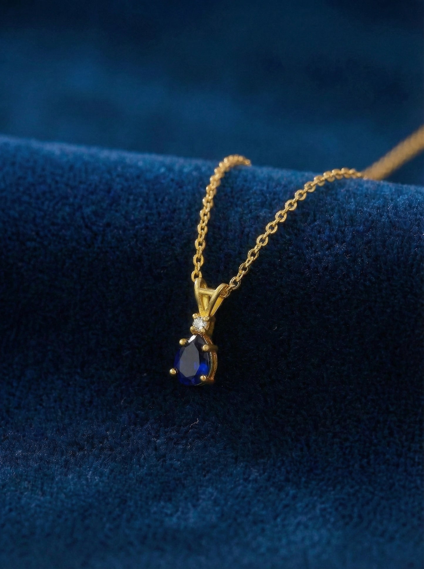 18k gold plated necklace with a blue gemstone pendant on a blue fabric background