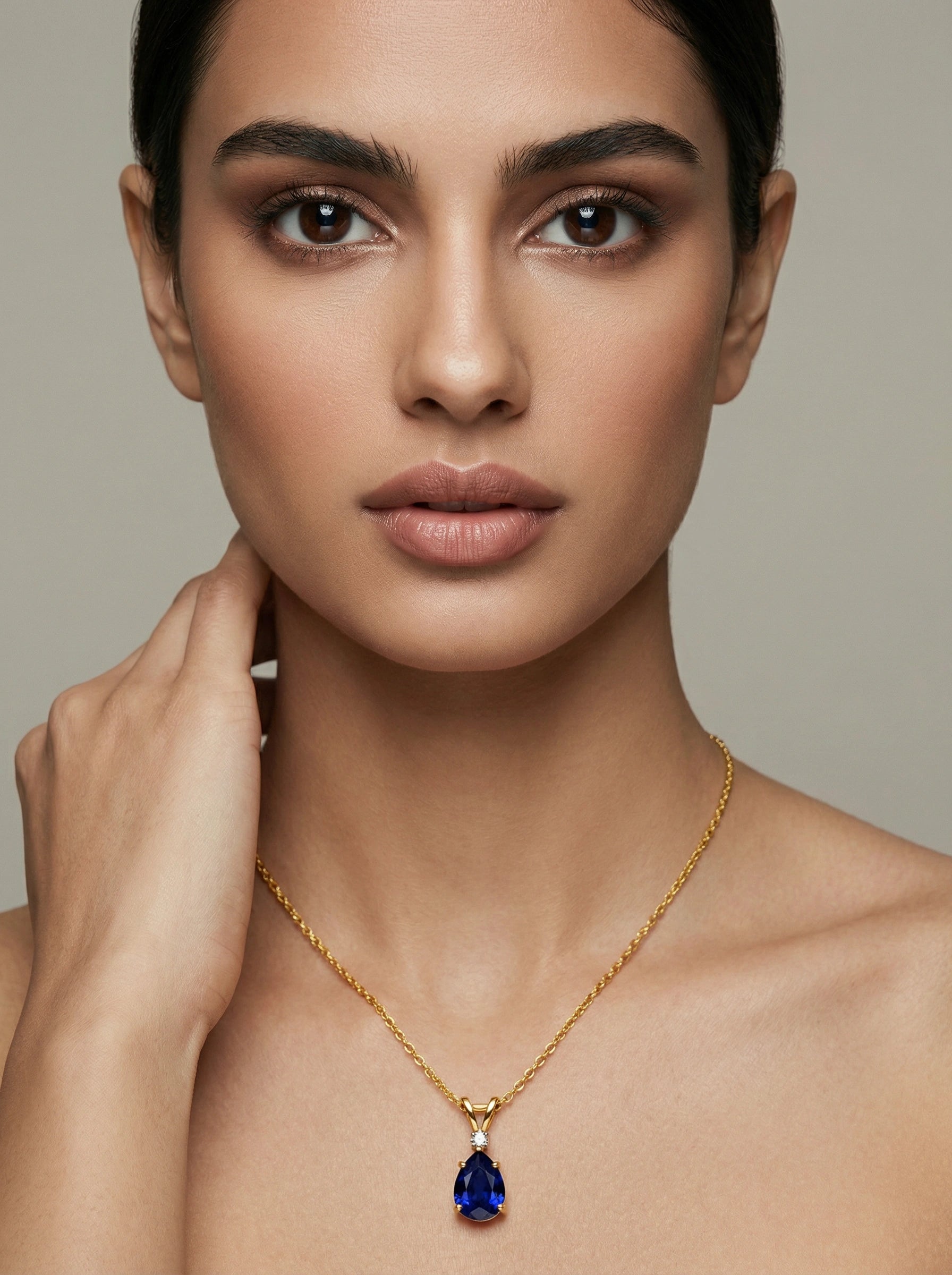 Woman wearing a 18k gold plated necklace with a blue pendant against a neutral background