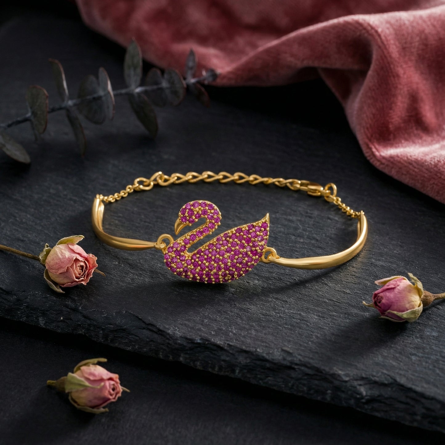 18k gold plated  bracelet with a pink swan design on a dark surface with flowers and a red fabric background.