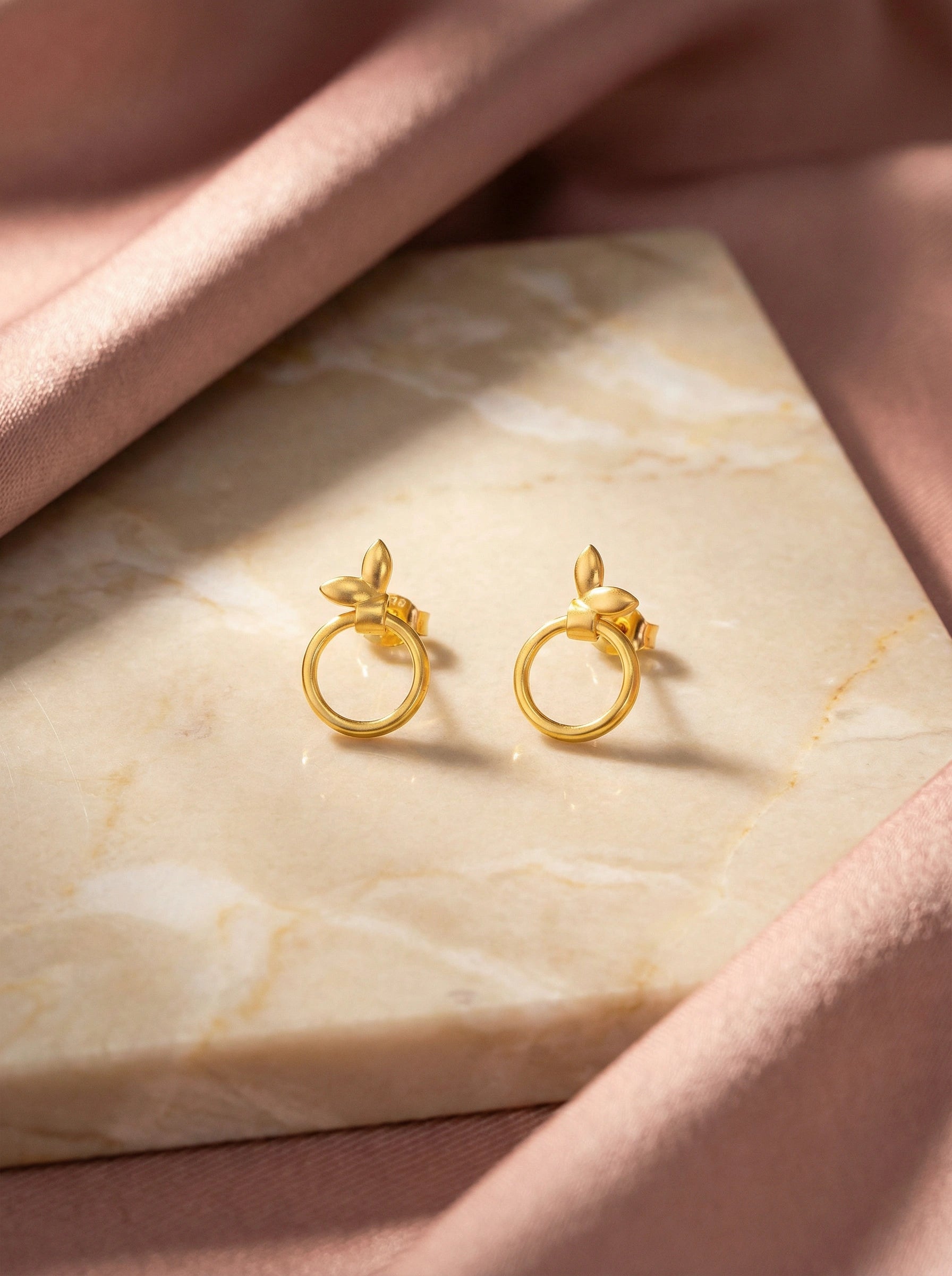 18k Gold plated earrings on a marble surface with a soft pink fabric background