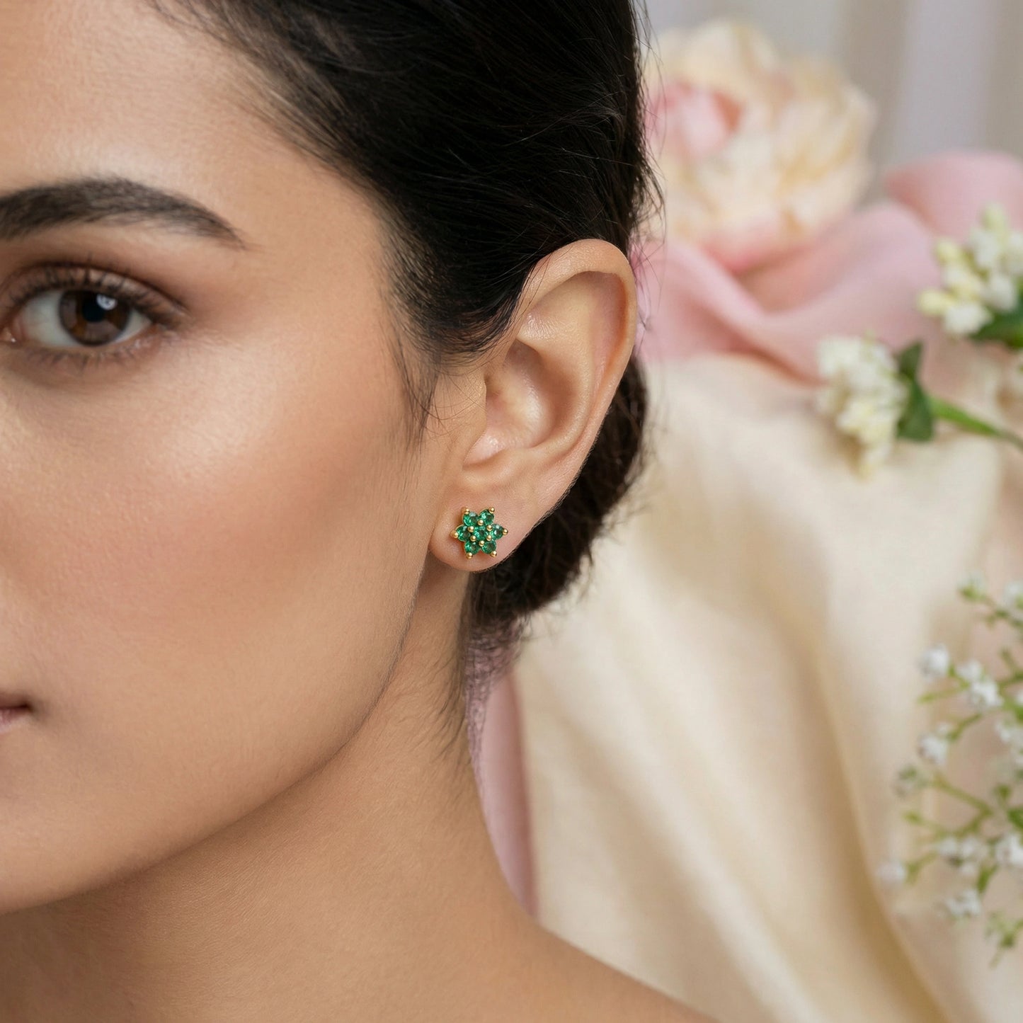 close-up of a woman wearing green 18k gold plated earrings with a blurred floral background