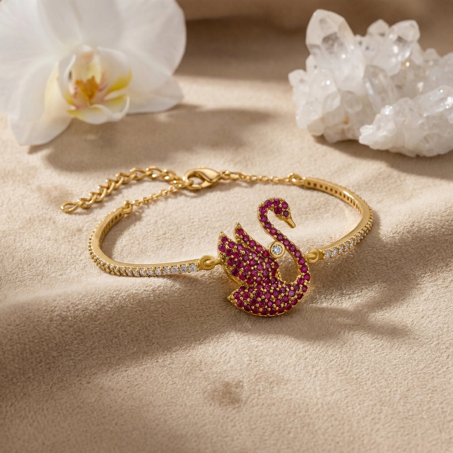 18k gold plated bracelet with a swan charm on a beige surface with flowers and crystals.