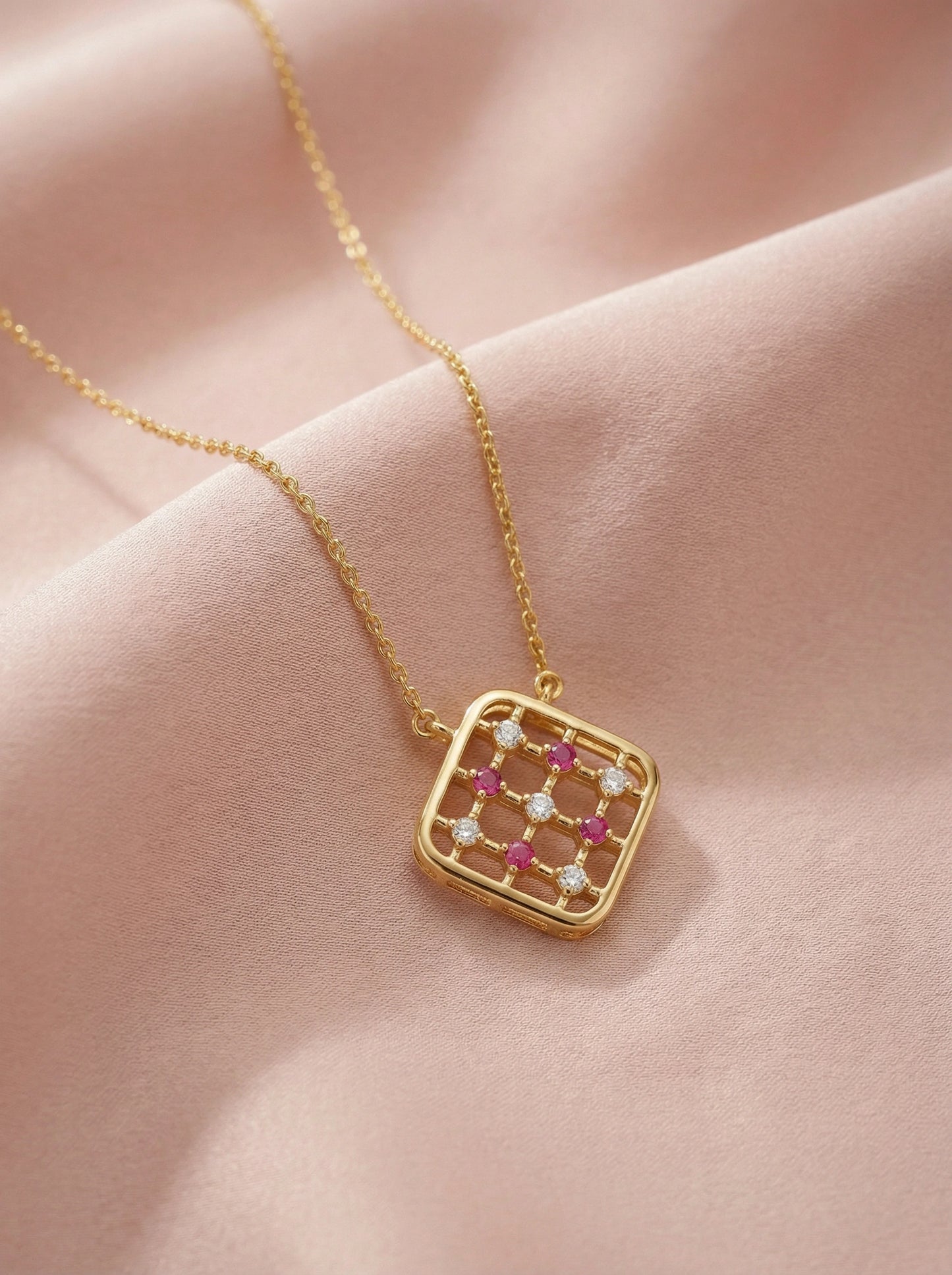 18k gold plated necklace with a square pendant featuring red and clear stones on a pink fabric background