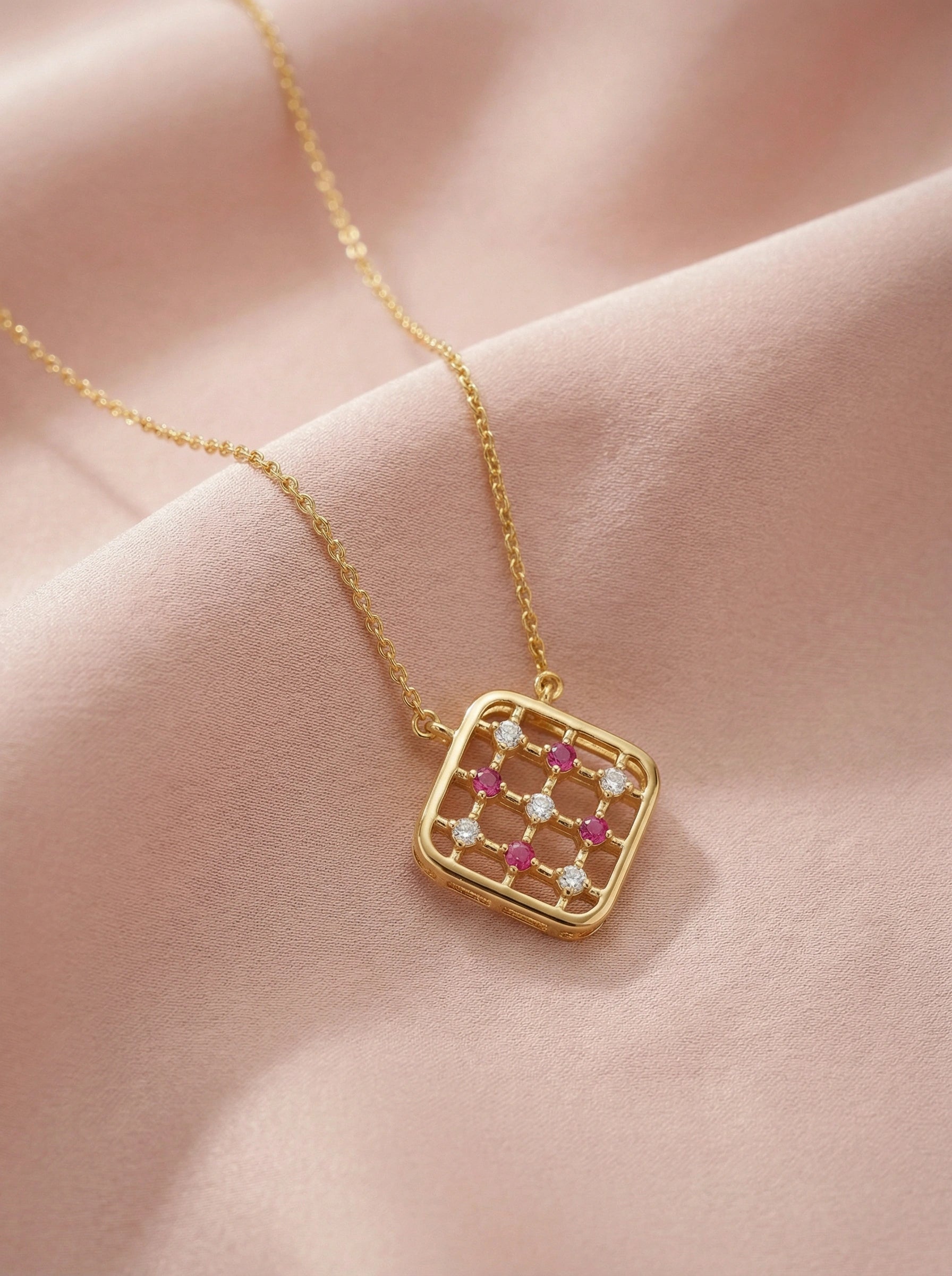 18k Gold plated necklace with a square pendant featuring red and clear stones on a pink fabric background