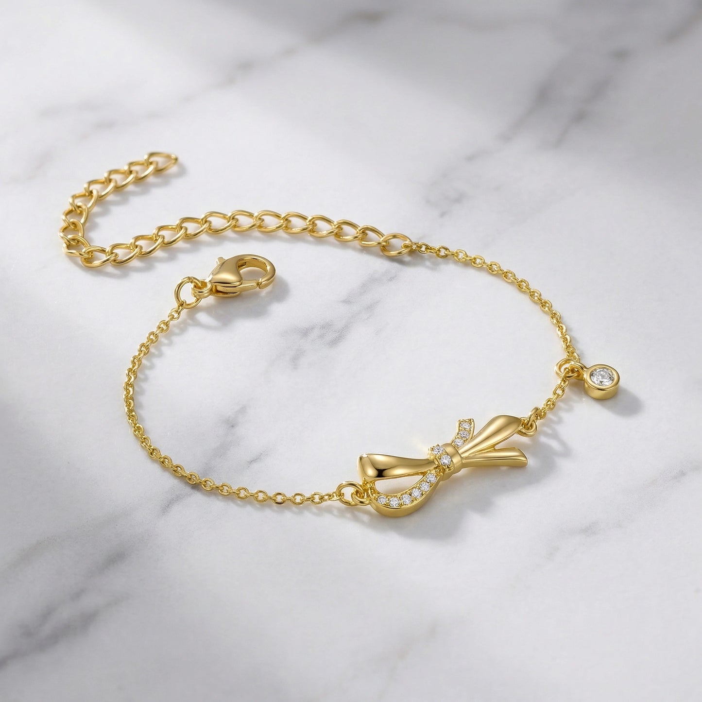 18k gold plated bracelet with bow charm on a marble background