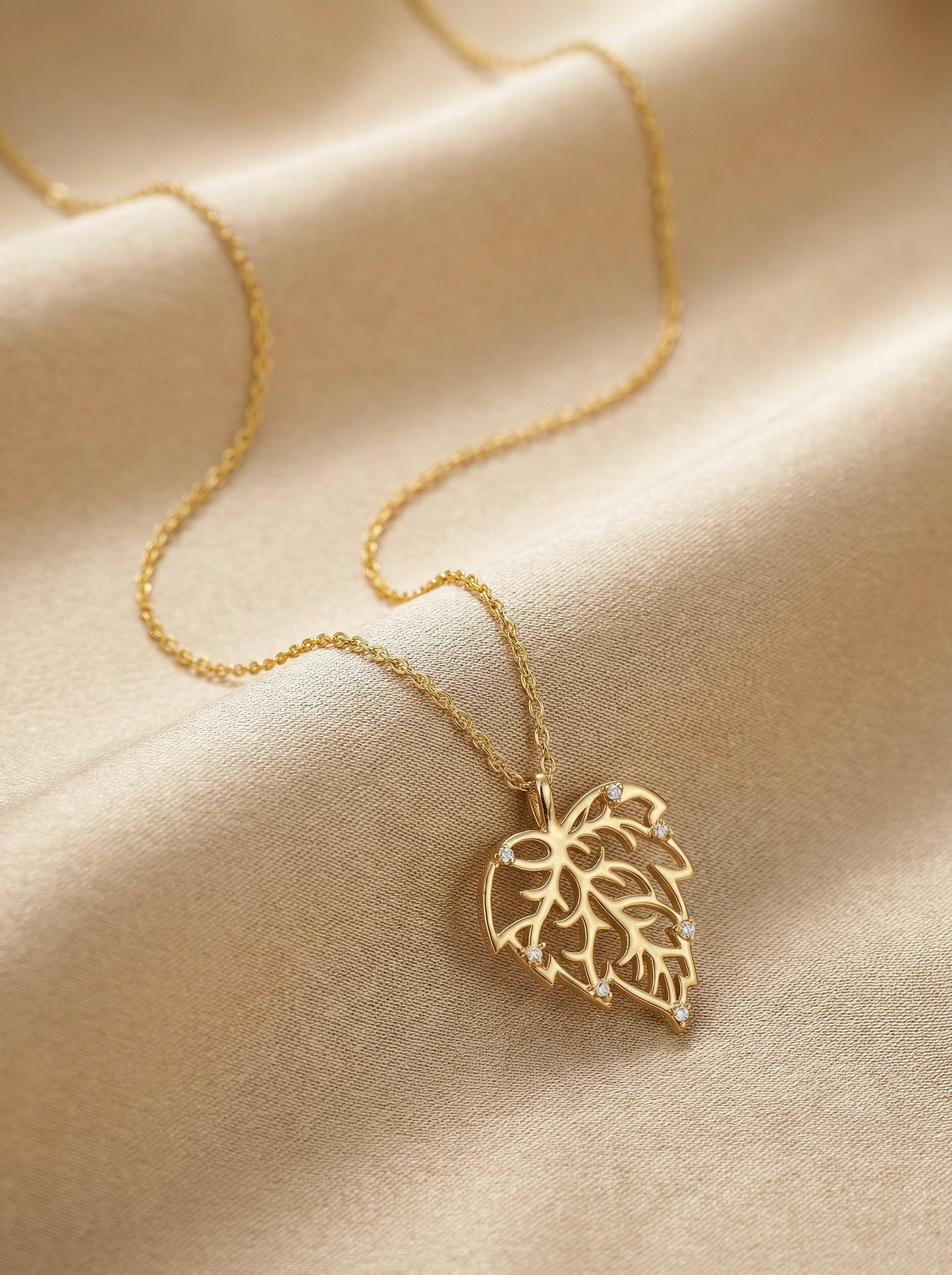 18k gold plated necklace with a leaf pendant on a beige fabric background