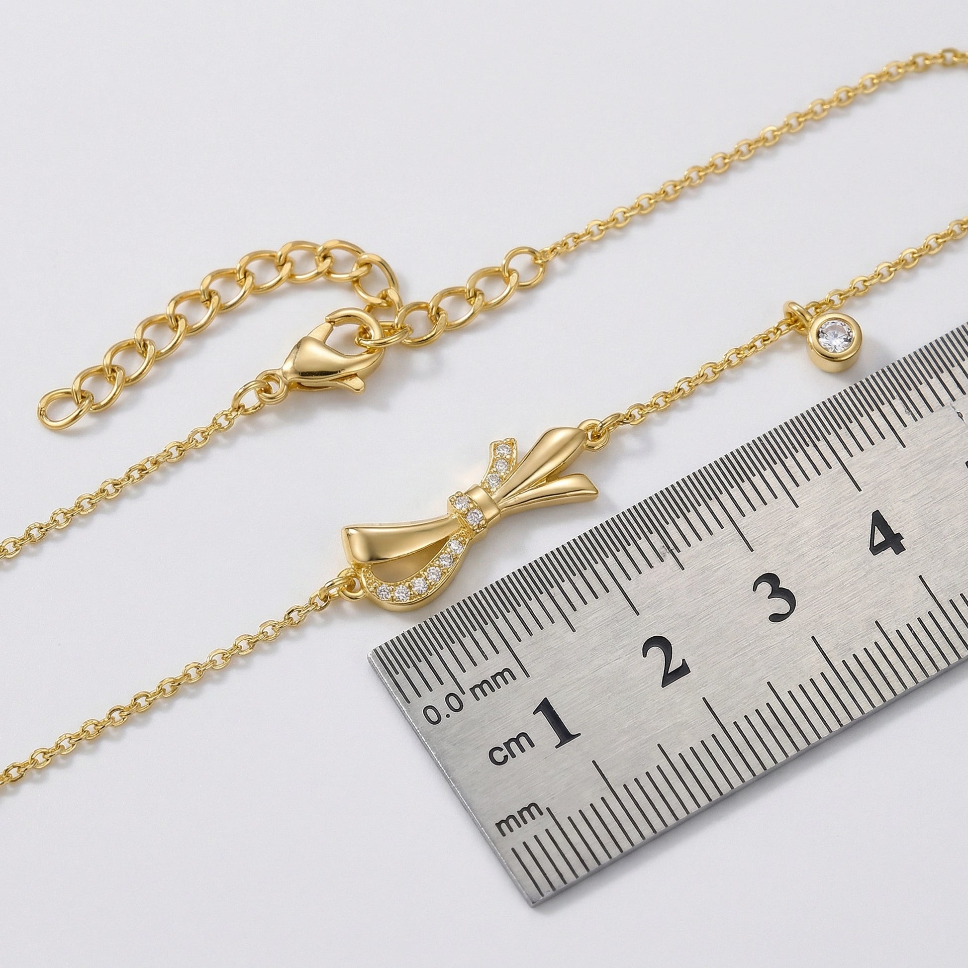 18k Gold plated bracelet with a bow charm next to a ruler for size reference on a white background