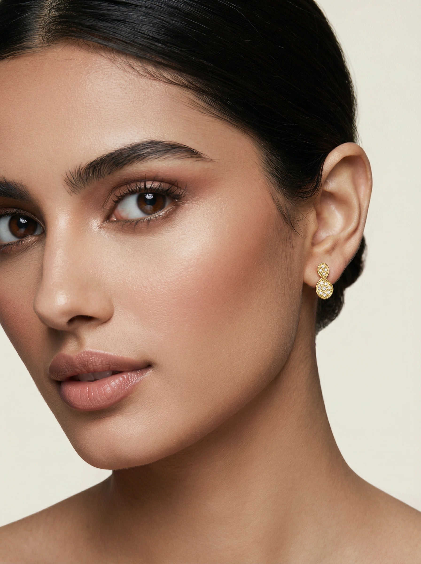 Close-up of a woman wearing 18k gold plated earrings with a neutral background