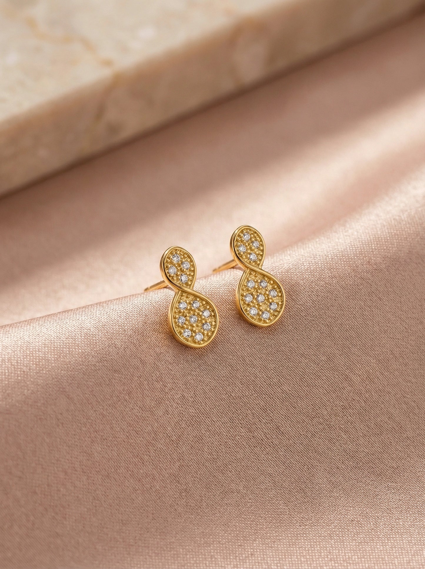 18k gold plated earrings with diamond accents on a soft pink fabric background