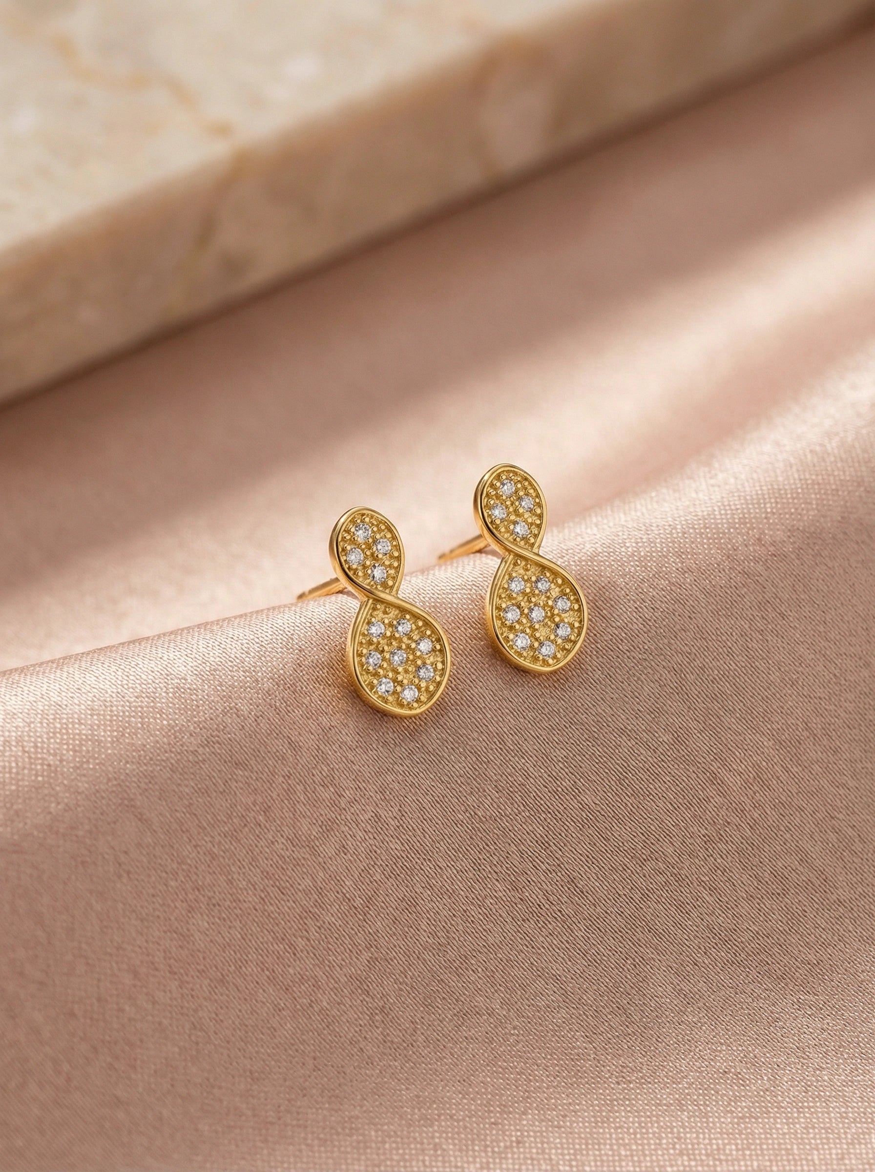 18k Gold plated earrings with diamond accents on a soft pink fabric background