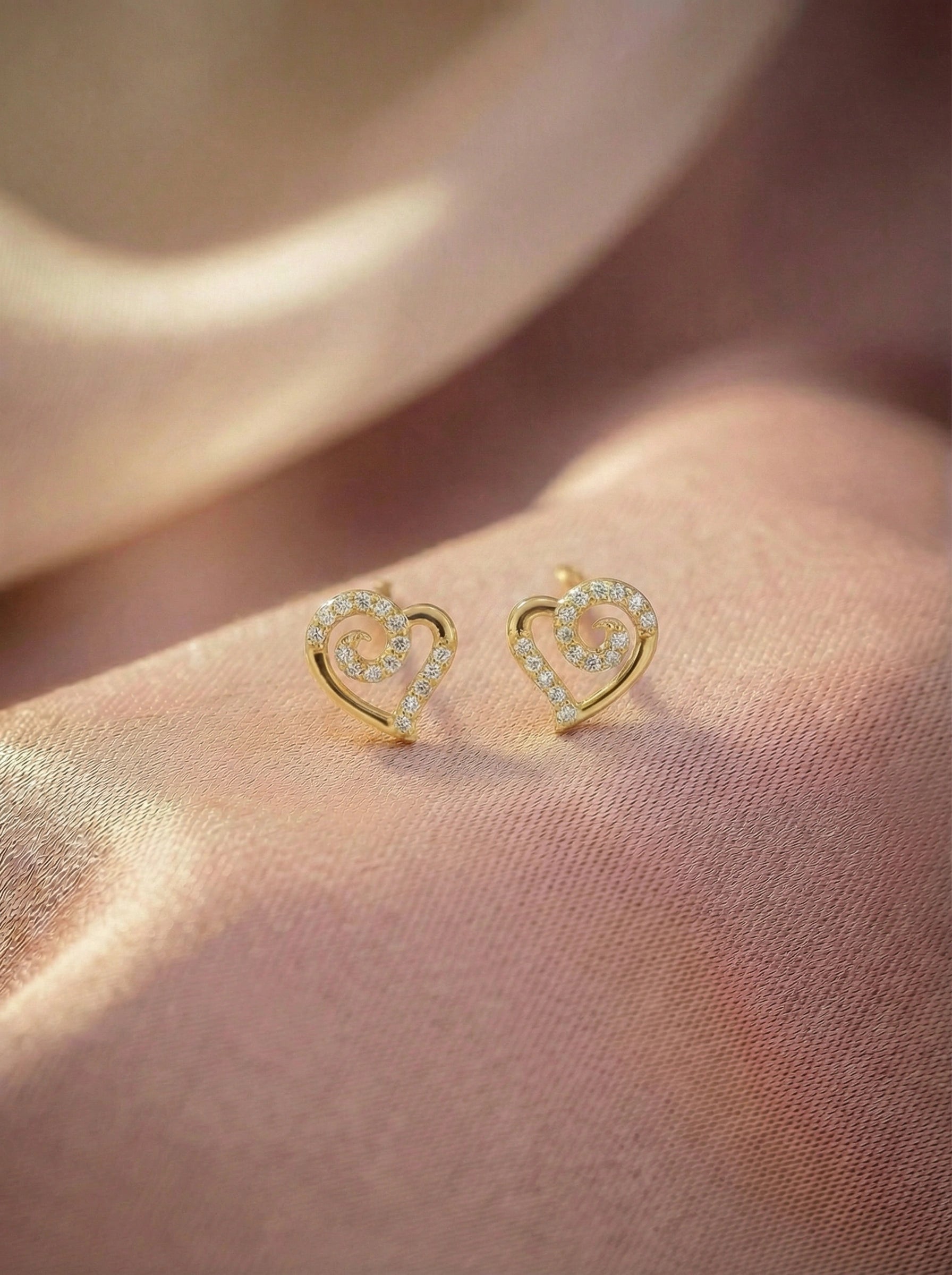 Heart-shaped 18k gold plated earrings on a soft pink fabric background