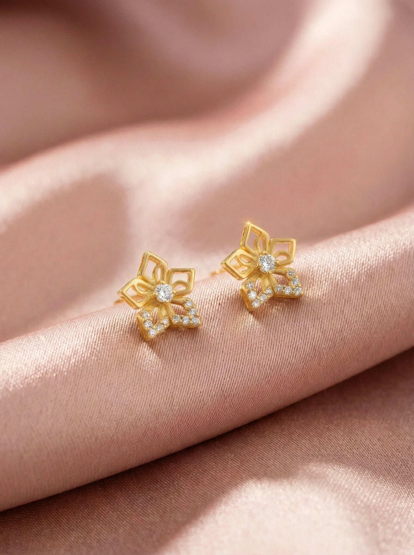 18k gold plated flower-shaped earrings with clear stones on a pink fabric background