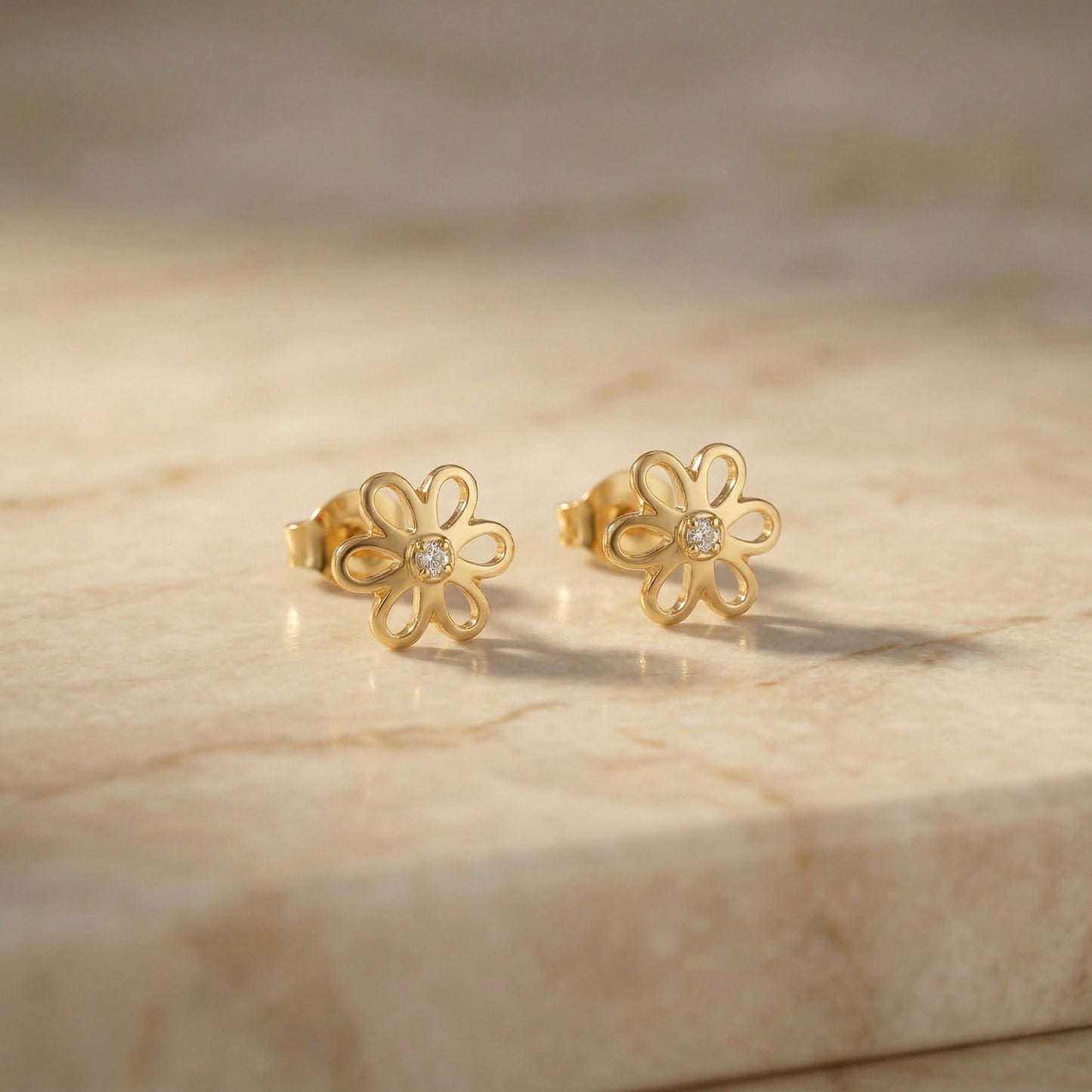 18k gold plated flower-shaped earrings with diamonds on a beige marble surface