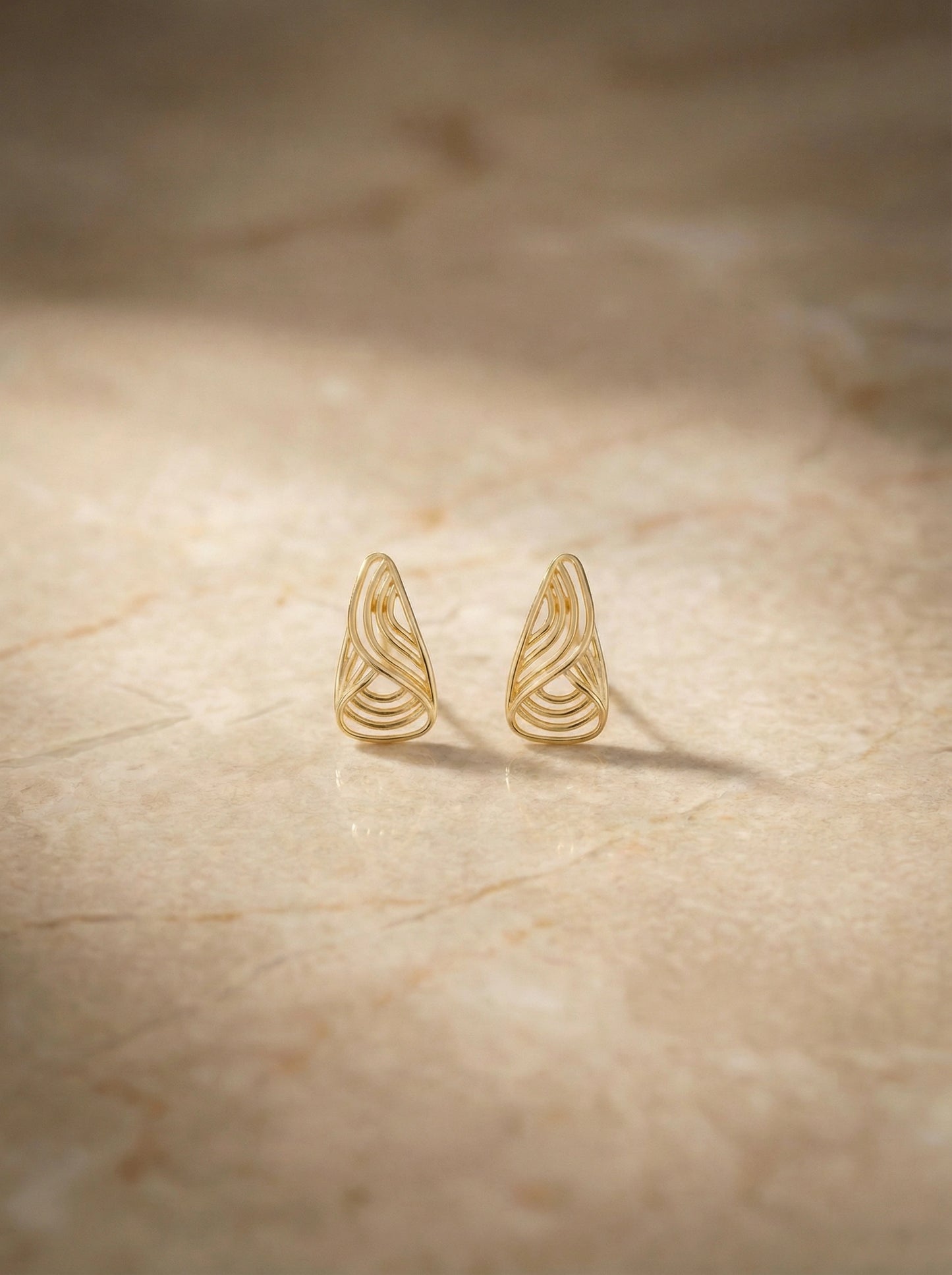 18k gold plated wing-shaped earrings on a beige surface